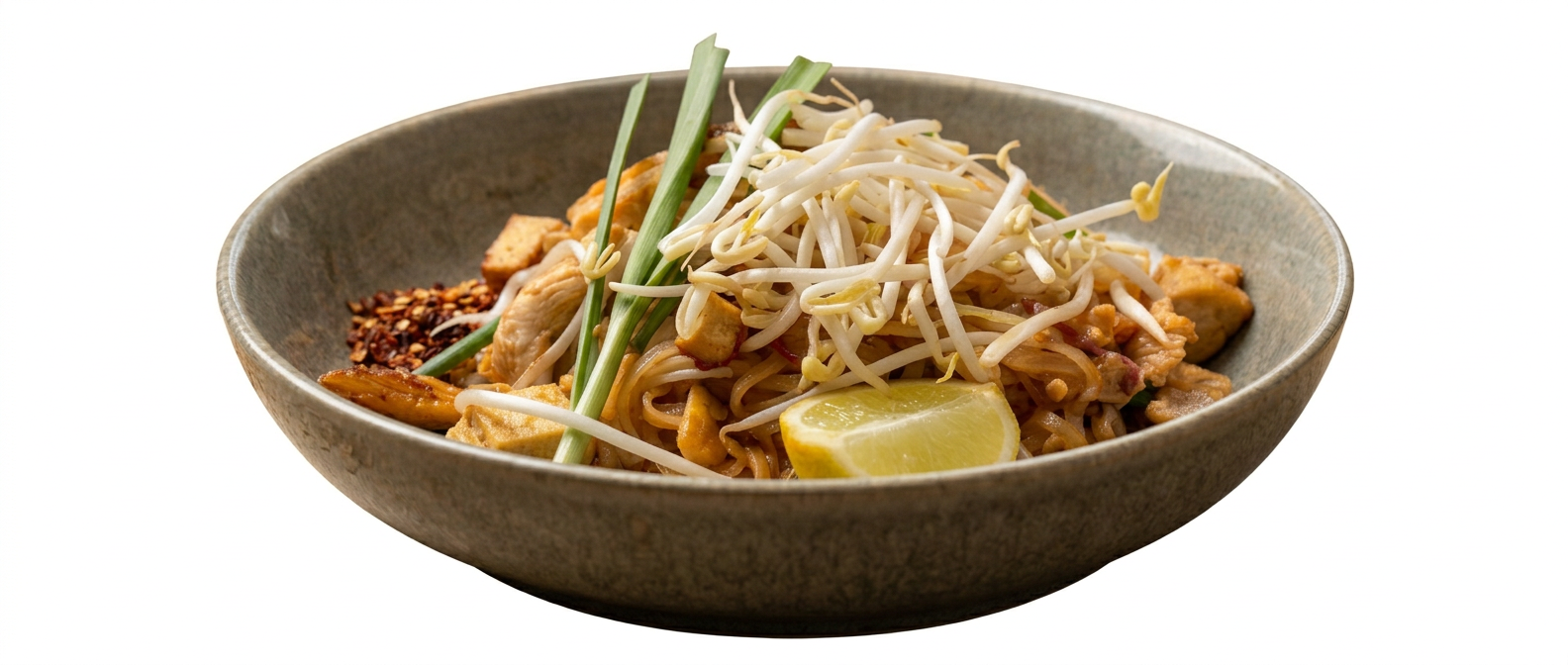 A bowl of stir-fried noodles with bean sprouts, green onions, tofu, and a lemon wedge.