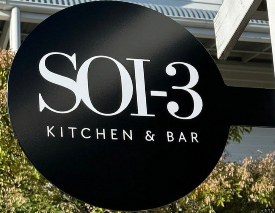Sign for SO3 Kitchen & Bar with black background and white text