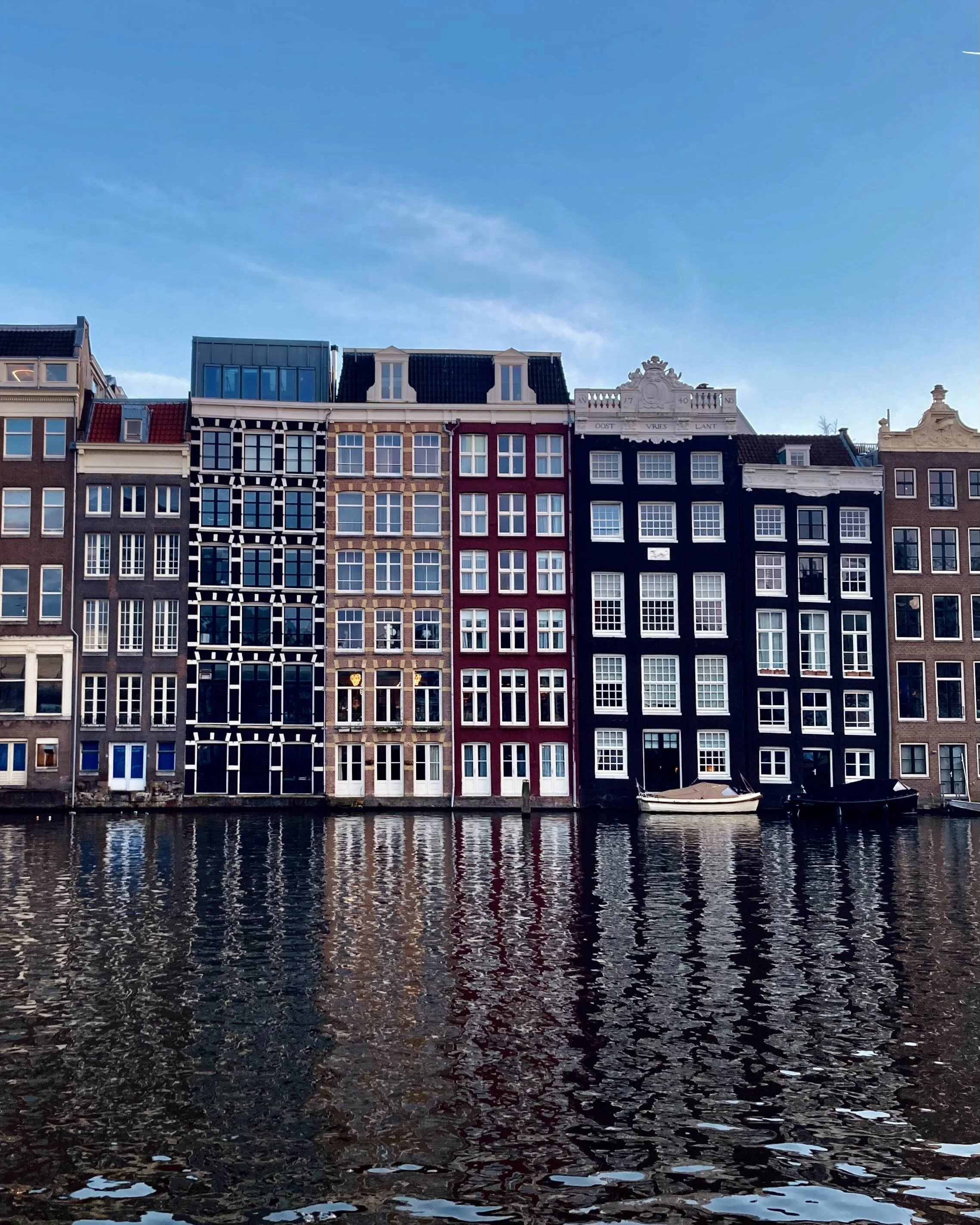 Amsterdam canal houses Colorful row of European-style buildings along a canal with calm water and a clear blue sky.