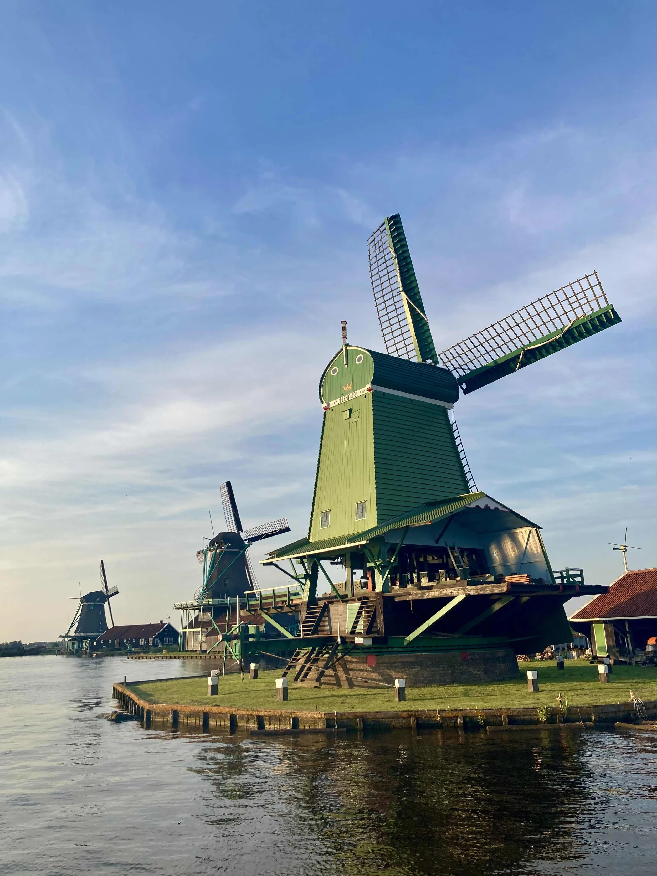 Multiple traditional Dutch windmills located along a waterway on a clear day with blue sky.