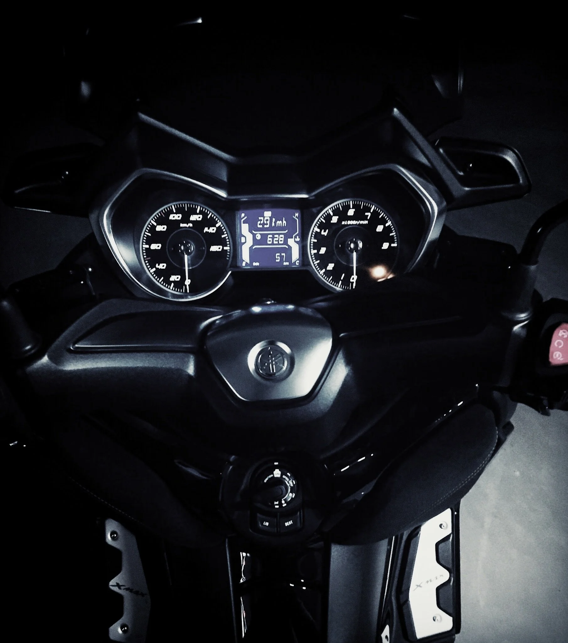 Digital motorcycle dashboard displaying speed, temperature, and fuel indicators, with a steering wheel and handlebars visible.