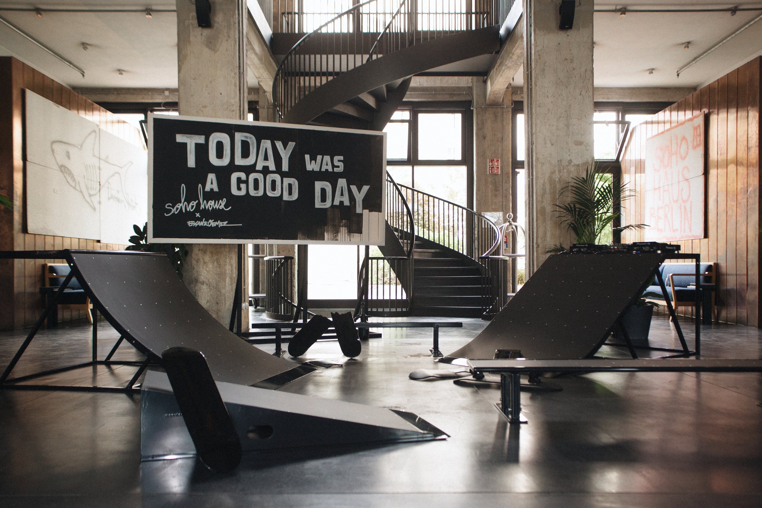 Ein eleganter, modern gestalteter Innenraum mit schwarzen Turnuchern, Sitzgelegenheiten und einer Treppe im Hintergrund, mit einer Tafel mit der Aufschrift 'Today was a good day' in der Mitte.