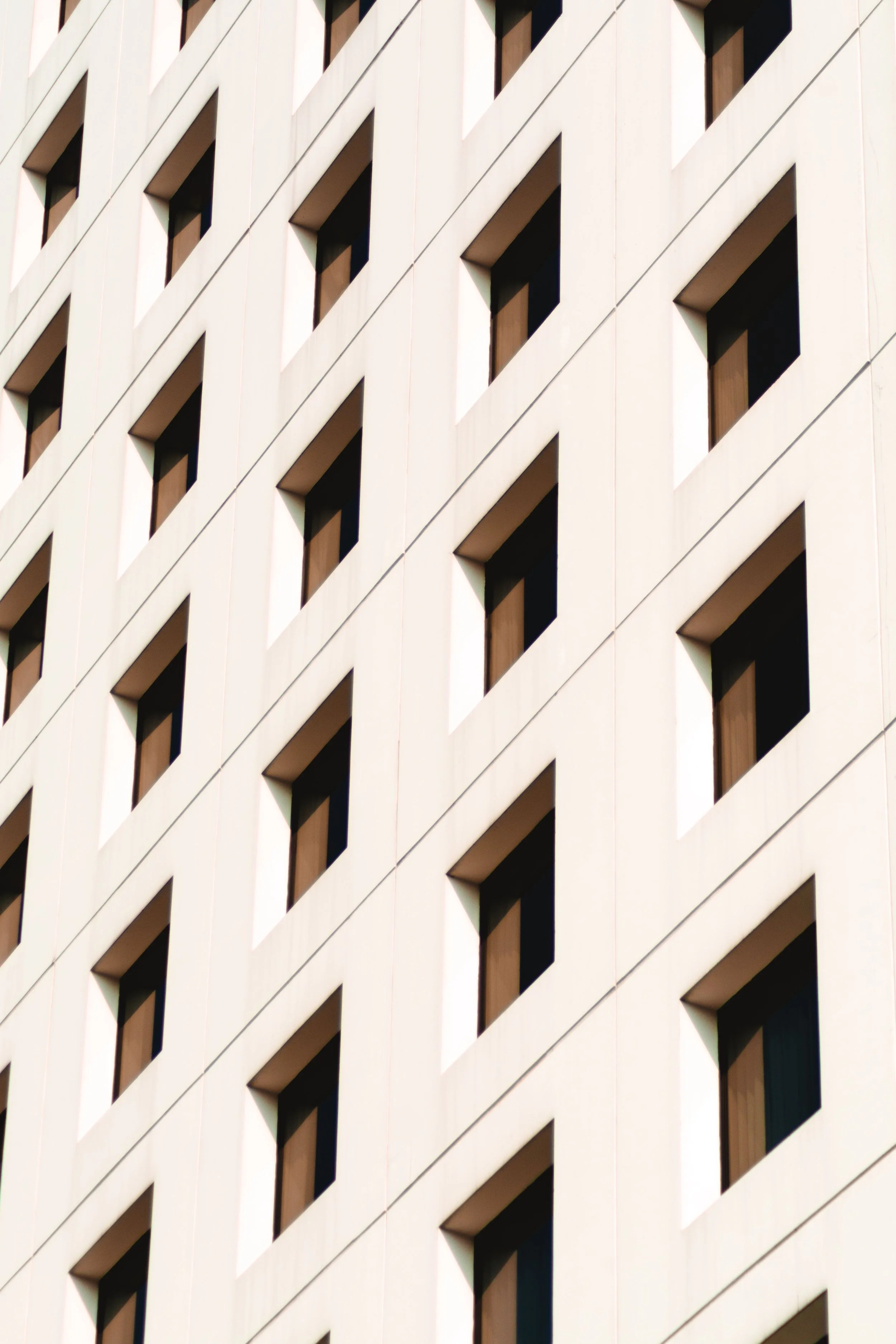 Close-up of a modern building exterior with a repeating pattern of vertical, rectangular windows and white walls, creating a geometric design.