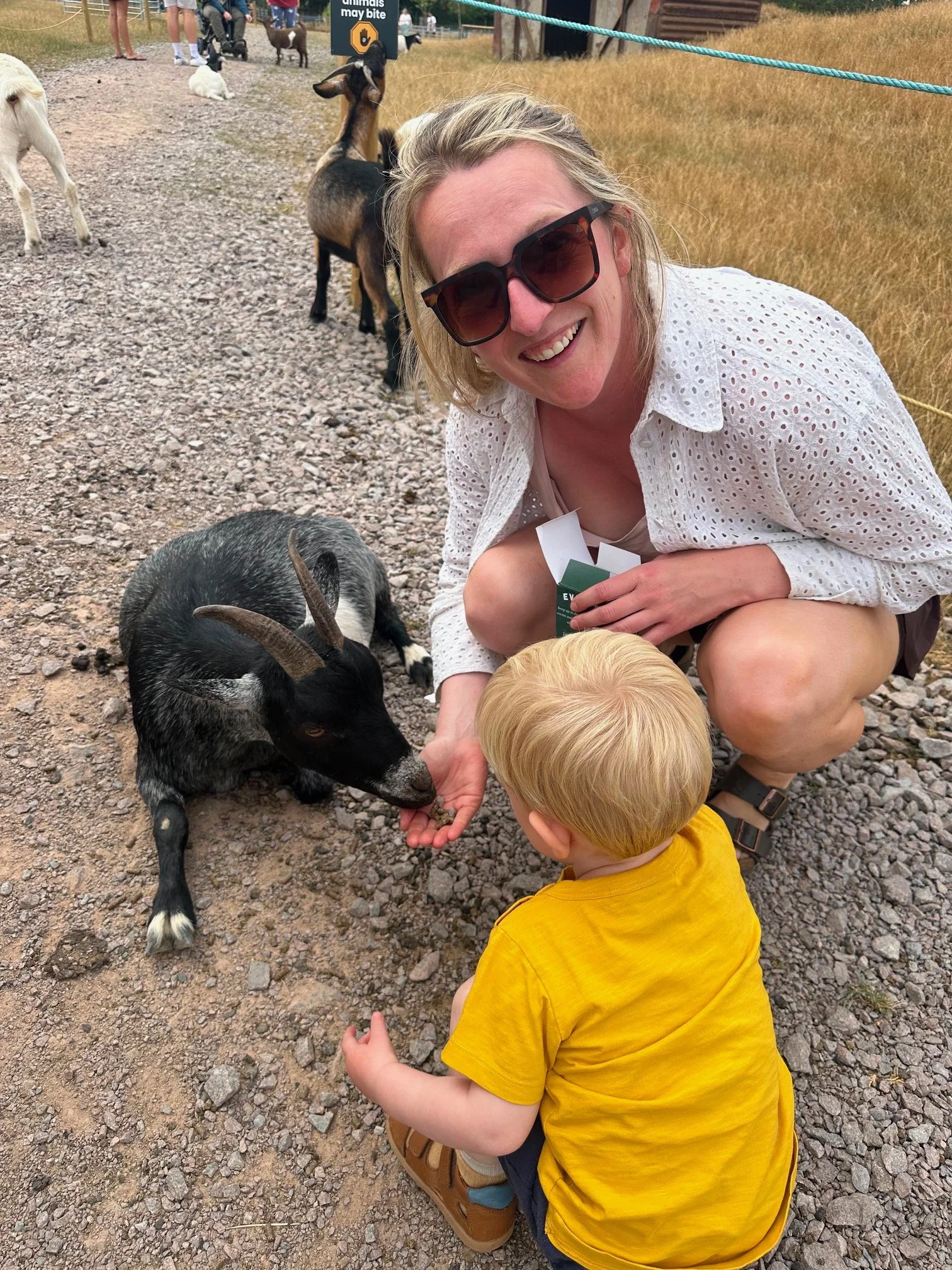 Blonde lady feeding a goat with her child