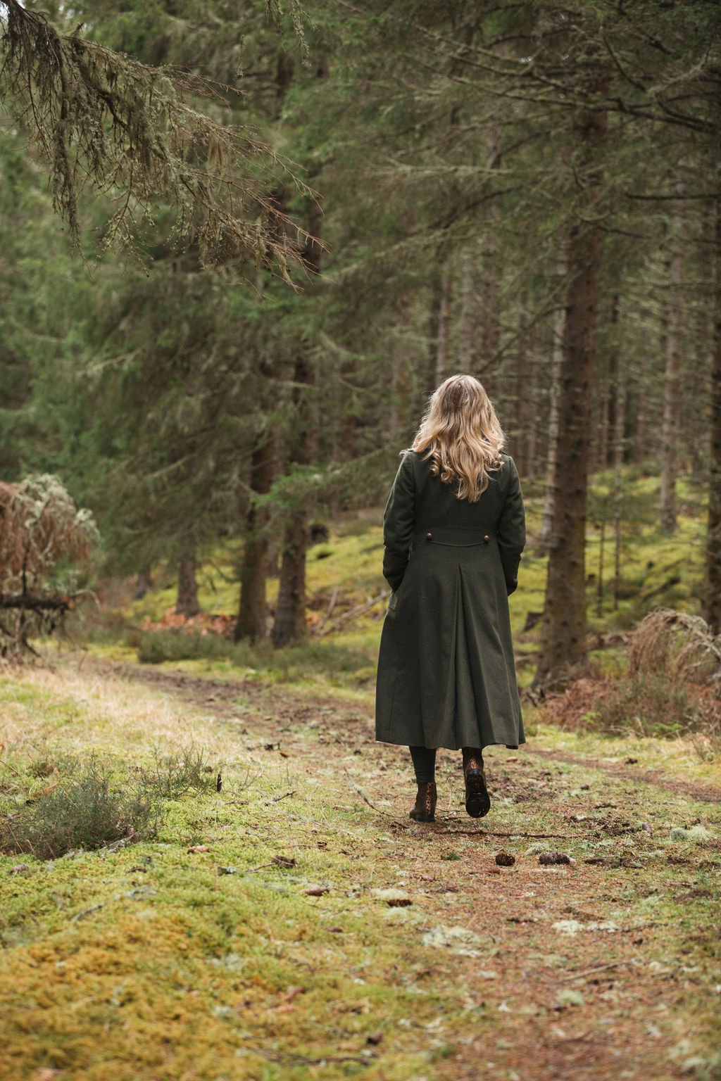 Lady in a green coat walking away down a forestry track