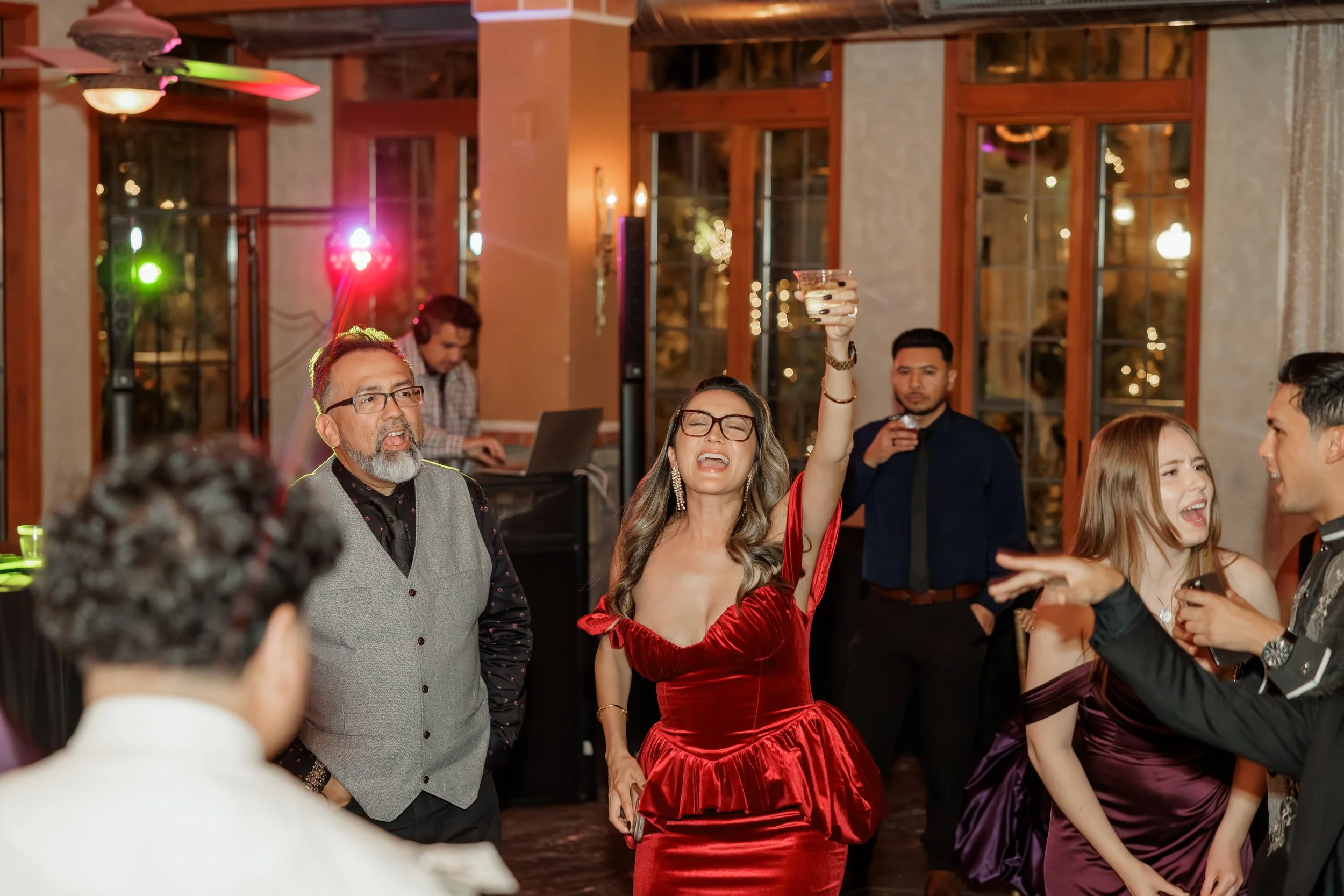 People dancing and enjoying themselves at a party in a warmly lit room with large windows.