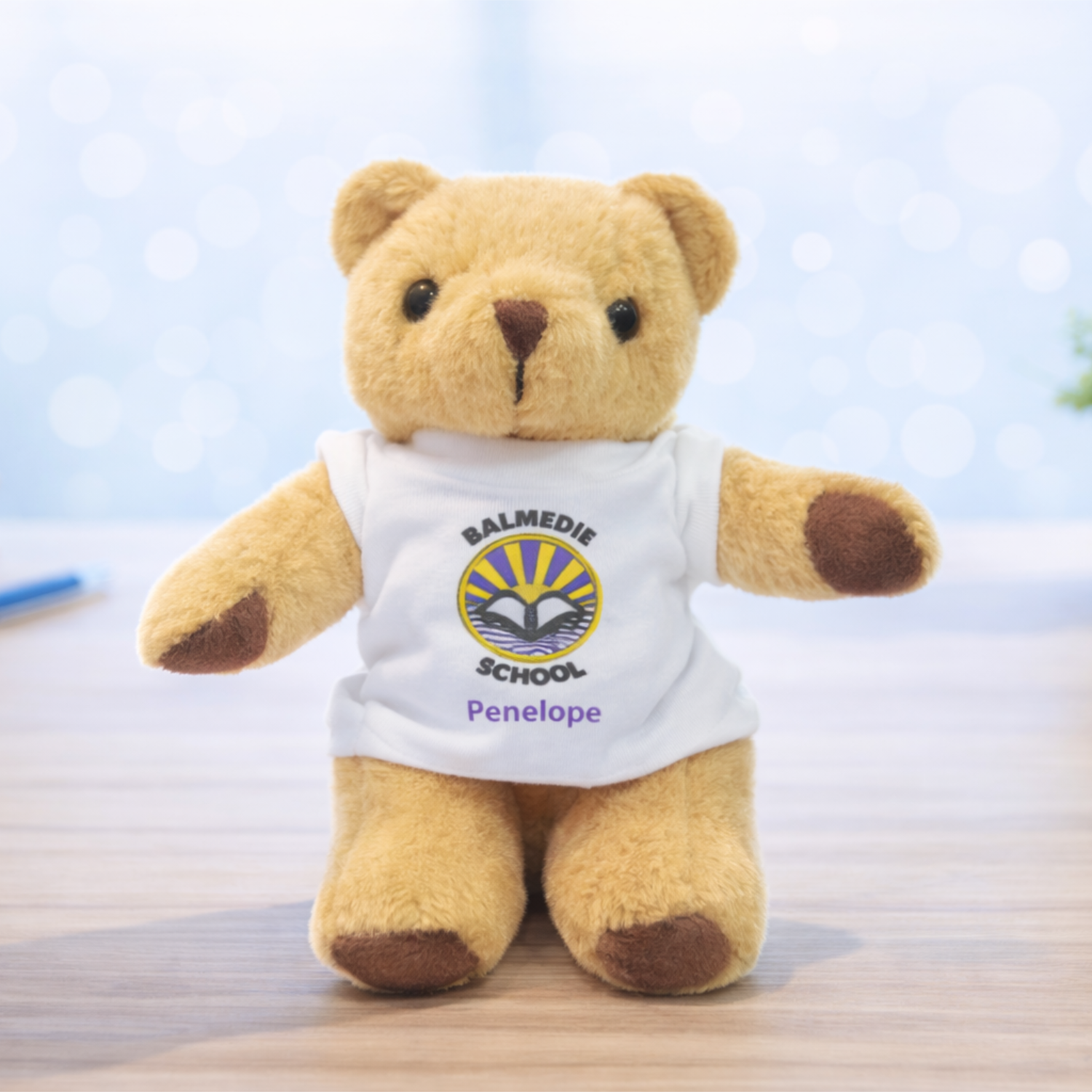 A tall - 25cm standing, teddy bear wearing a white t-shirt with a school logo printed in full colour