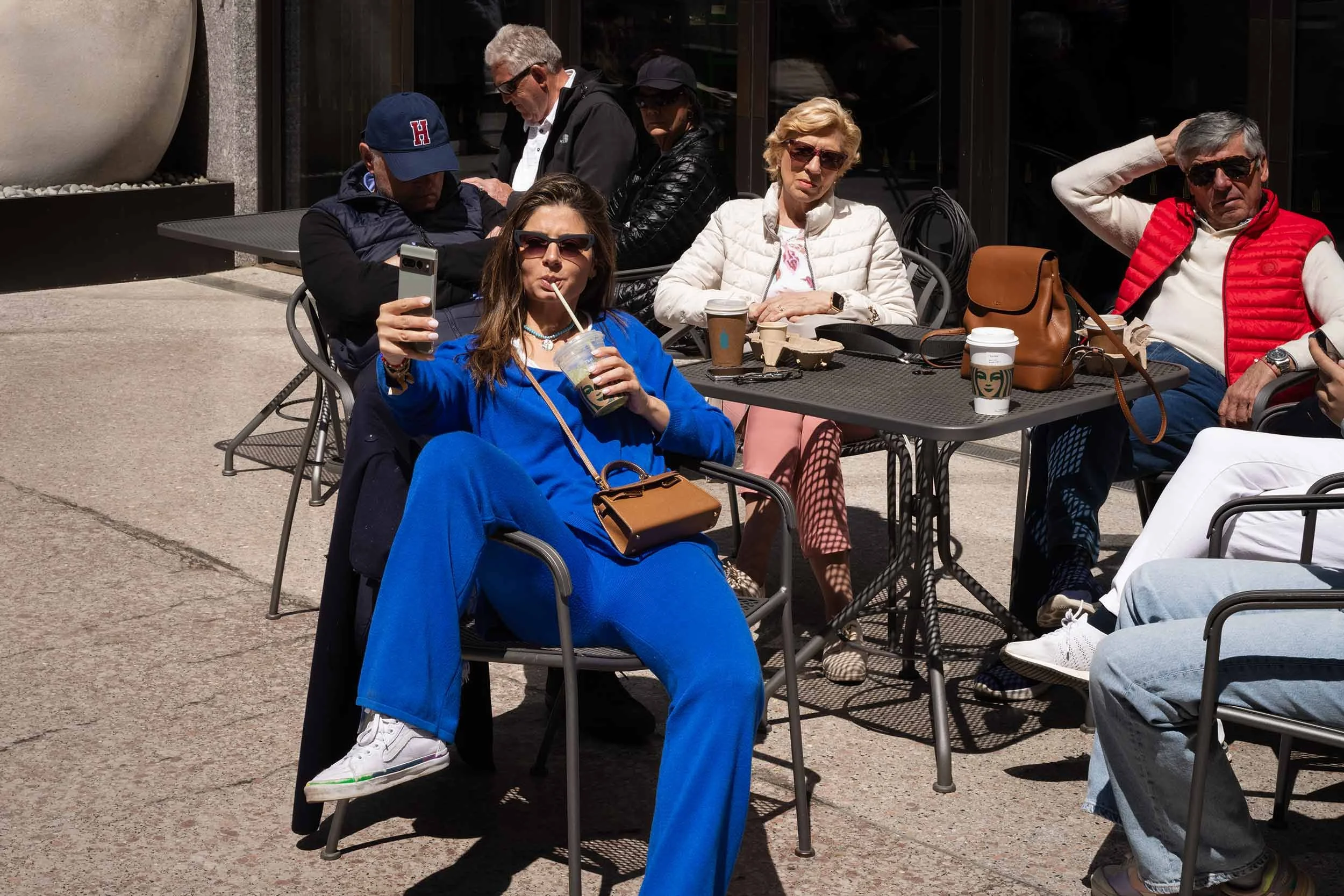 Eine Frau in leuchtend blauer Kleidung fotografiert sich selbst mit dem Smartphone und trinkt dabei aus einem Becher in einem New Yorker Straßencafé.