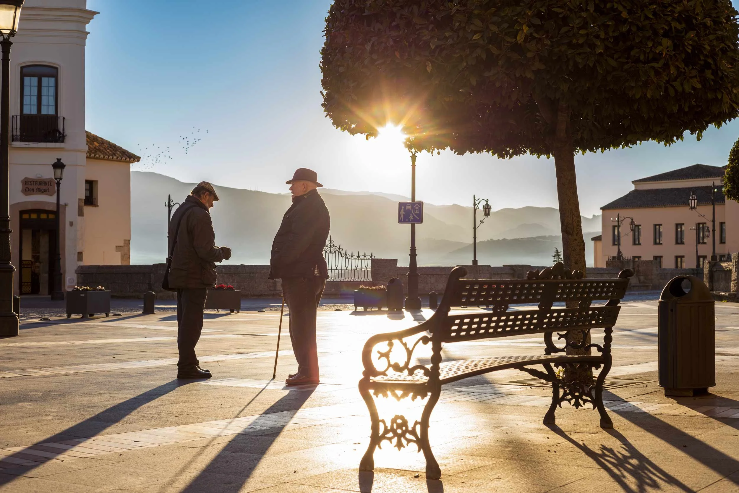 Das Bild zeigt zwei ältere Männer im Gespräch vor dem Sonnenaufgang in Ronda, mit Blick auf die berühmte Puente Nuevo.