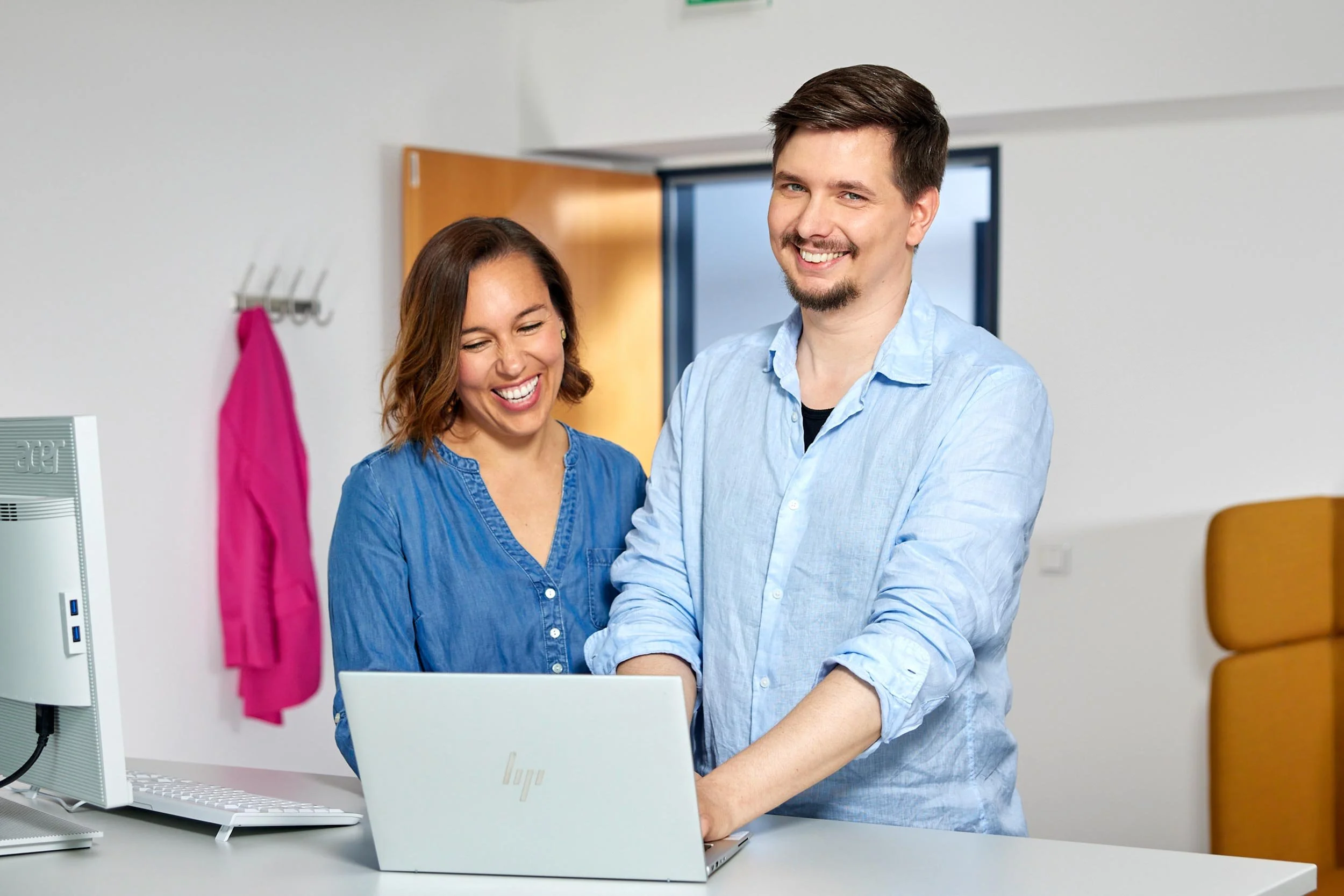 Zwei Personen stehen an einem Tisch in einem Büro und arbeiten gemeinsam an einem Laptop.
