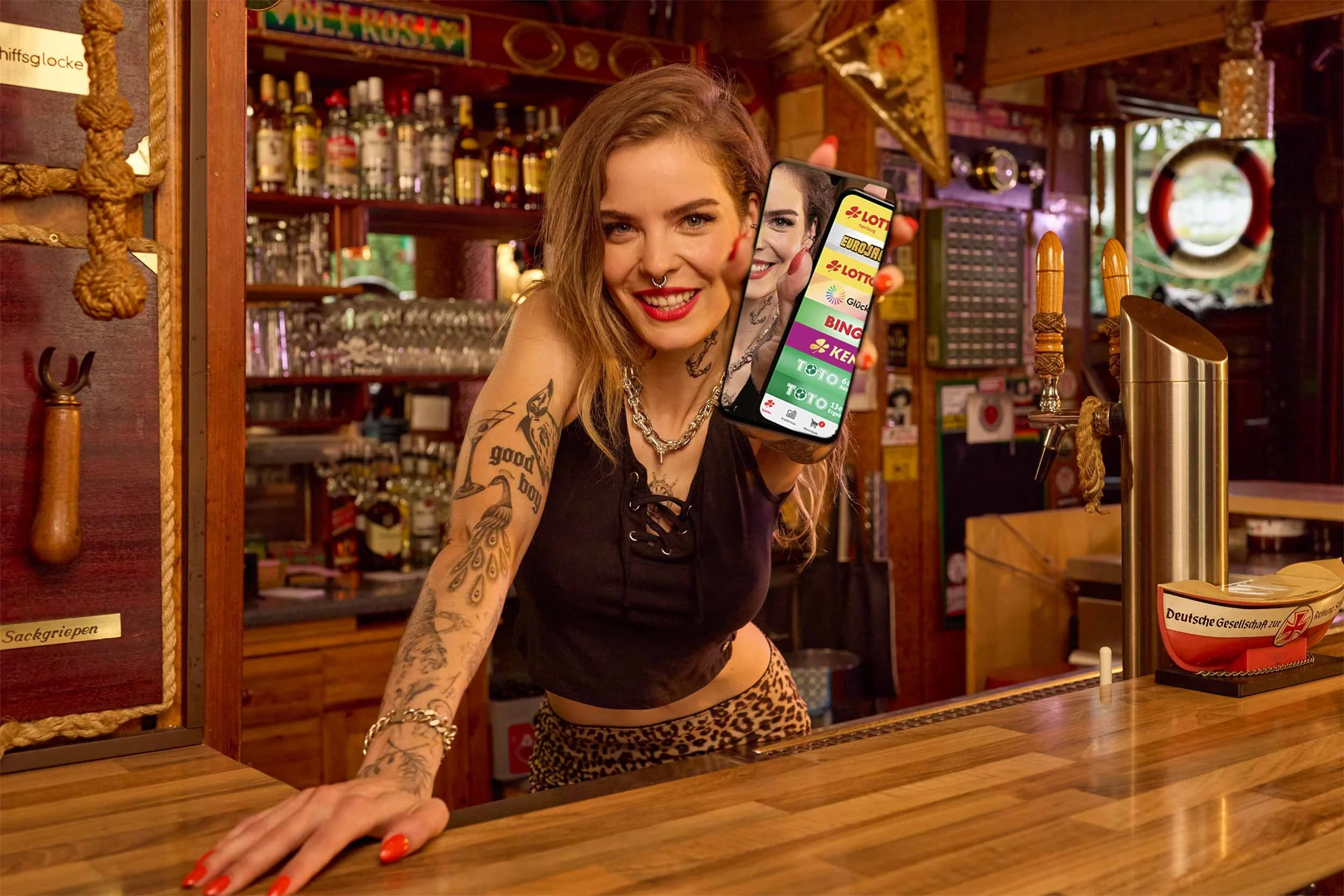 Barkeeperin mit Smartphone und Lotto-App hinter einer Bar