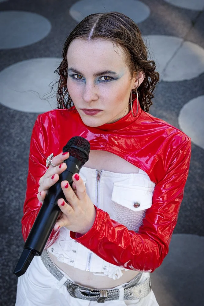 Mitglied der Band III RIØT hält ein Mikrofon und blickt in die Kamera. Aufnahme vor dem Futurium in Berlin.