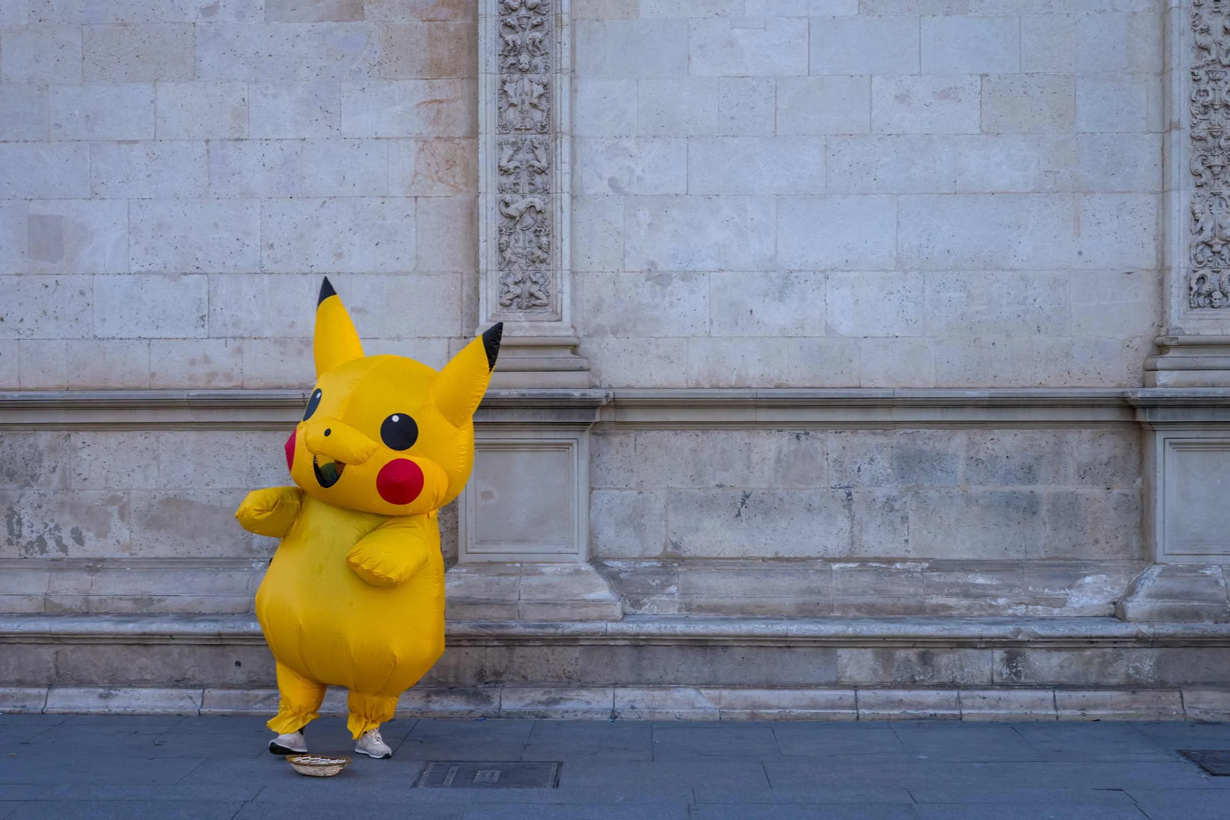 Person im gelben pikachu kostuem steht vor einer steinernen fassade in sevilla