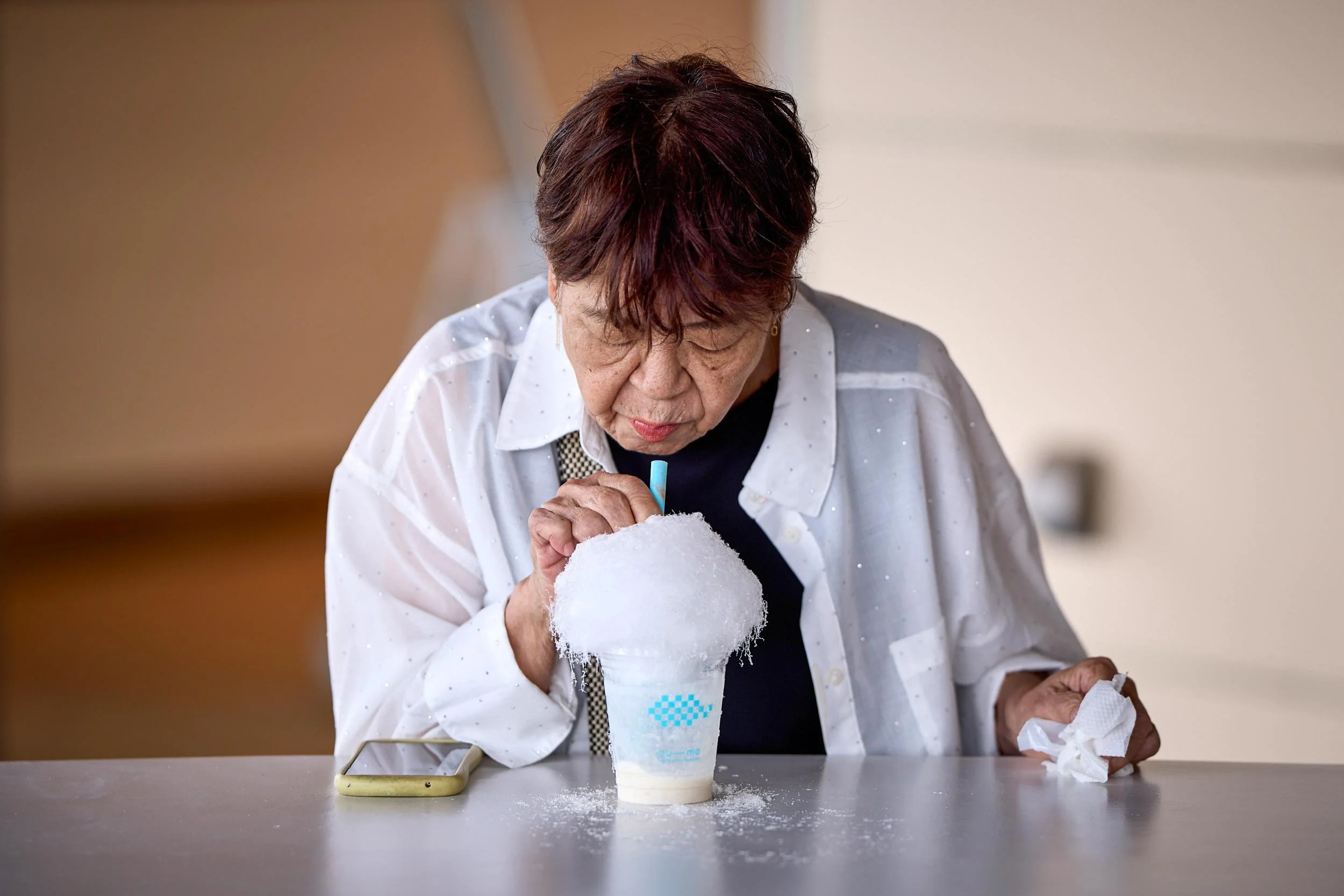 Ältere Frau sitzt an einem Tisch in der Sōunzan Station und isst ein Eis oder Dessert aus einem Becher.