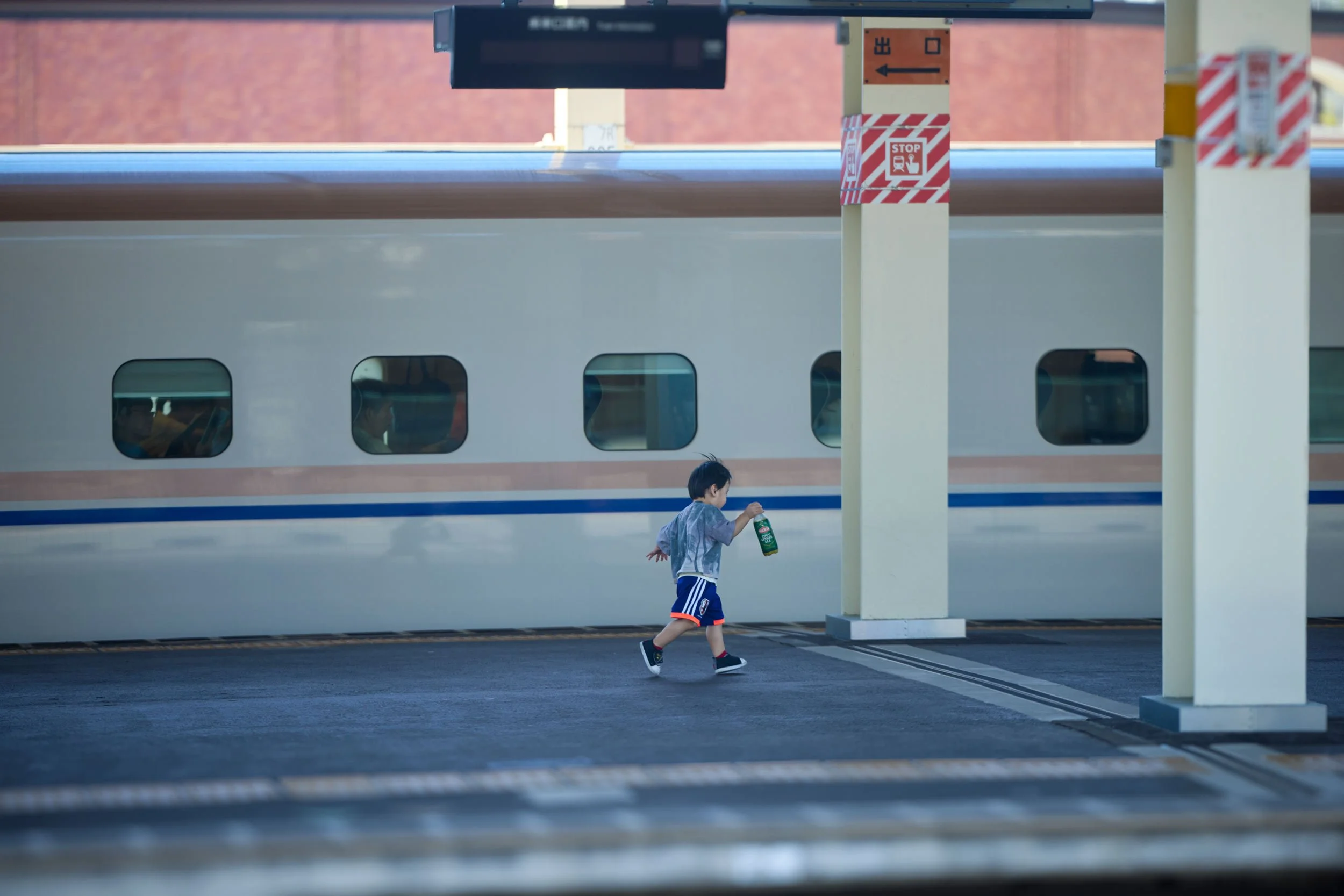 Kleines Kind läuft über einen Bahnsteig und hält eine grüne Getränkeflasche, im Hintergrund steht ein Zug.