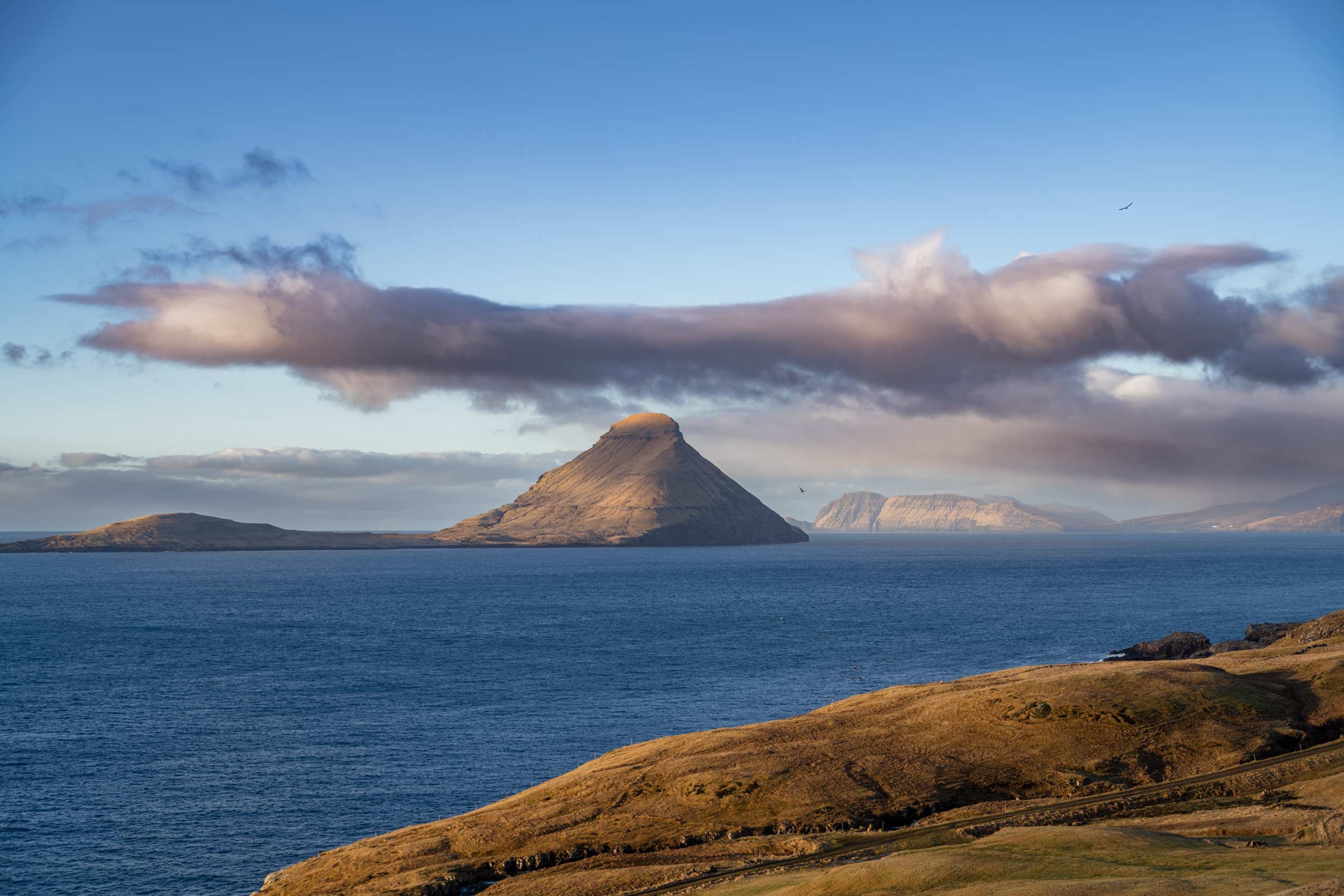 Insel mit steilem berg ragt aus dem meer, weitere inseln im hintergrund, faeroer
