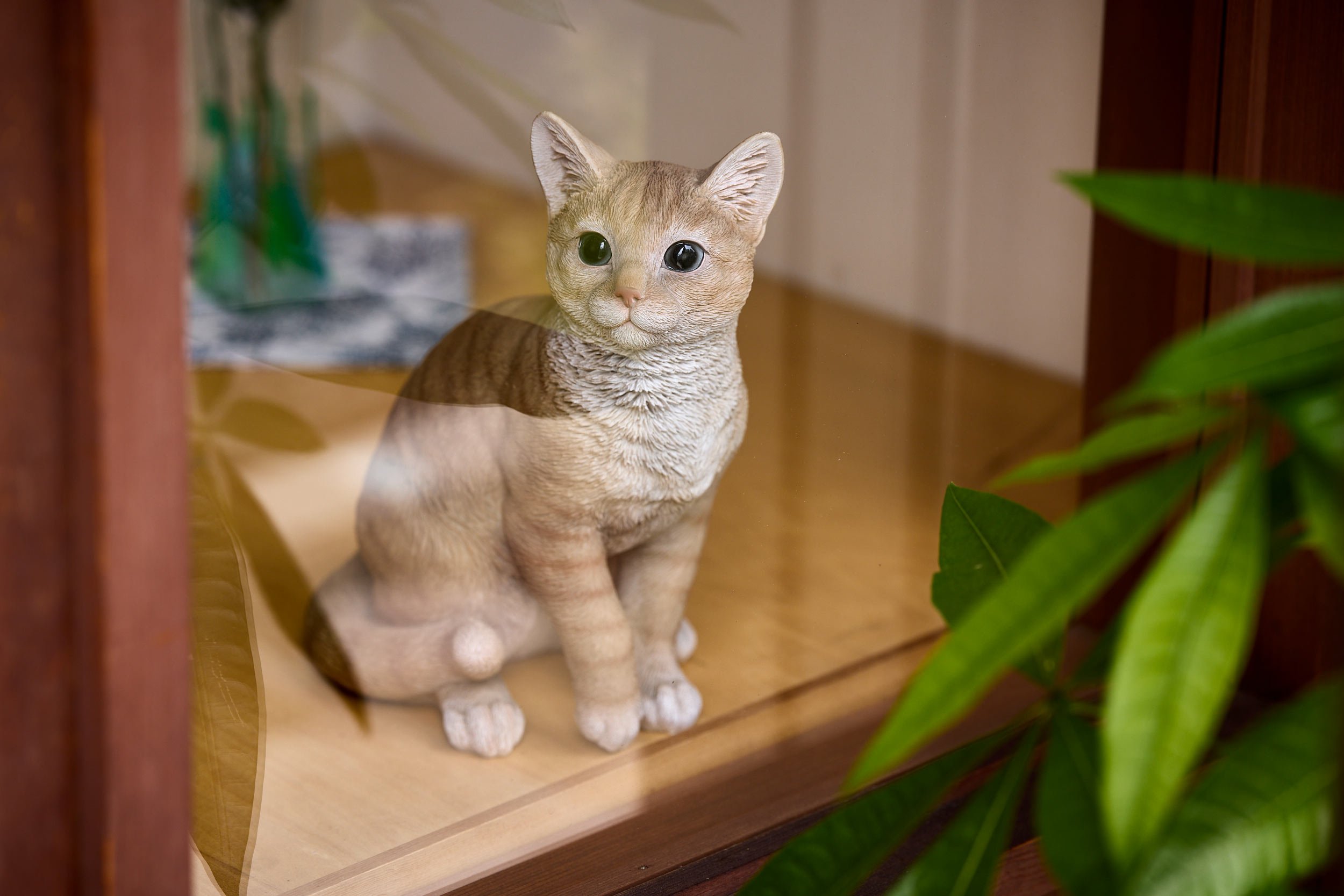 Katzenfigur sitzt im Schaufenster hinter Glas neben Pflanzen. Tokio