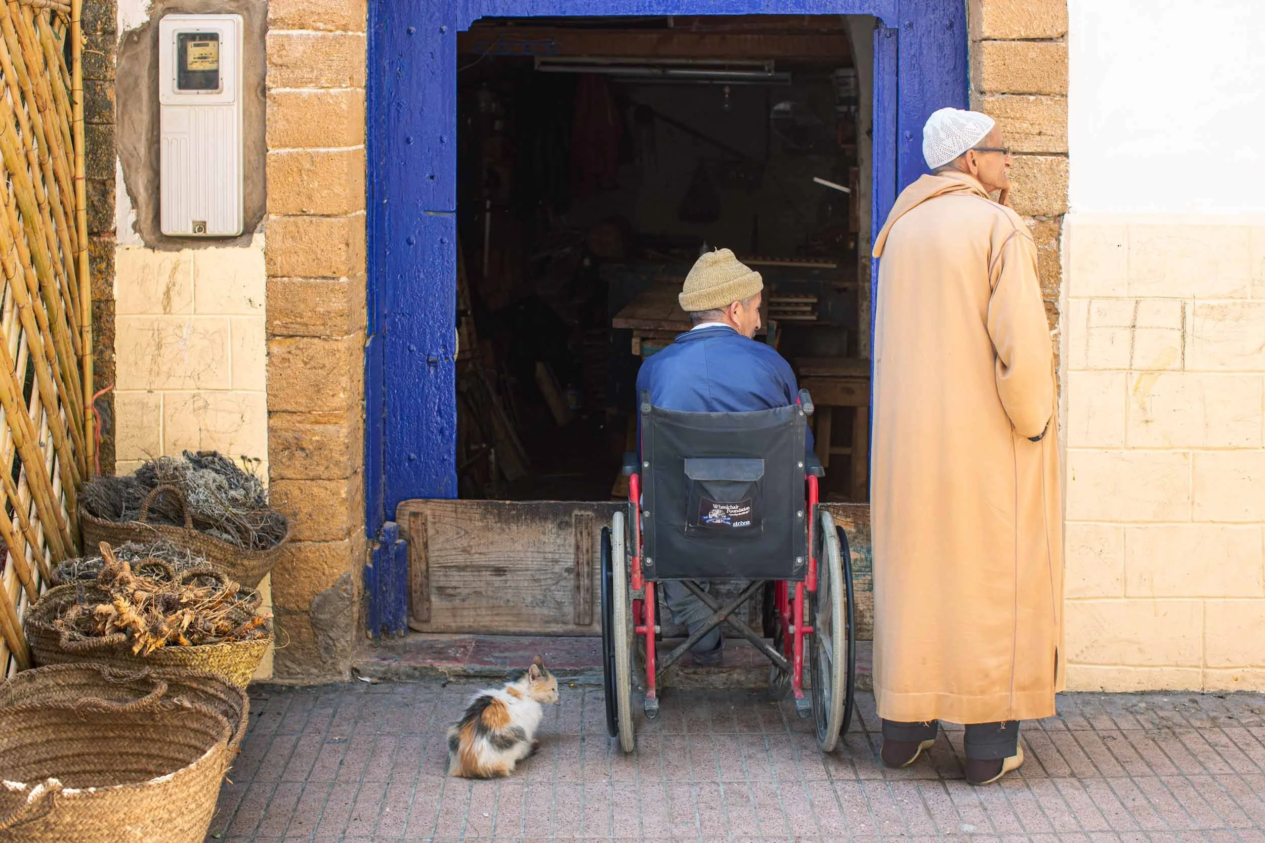 Mann im rollstuhl sitzt im eingang einer werkstatt, daneben steht ein weiterer mann, marokko