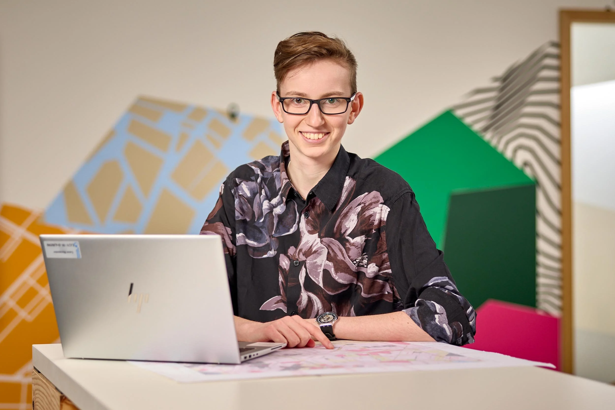 Auszubildende im Bereich Geodatenanalyse mit Laptop und Plänen an einem Arbeitsplatz