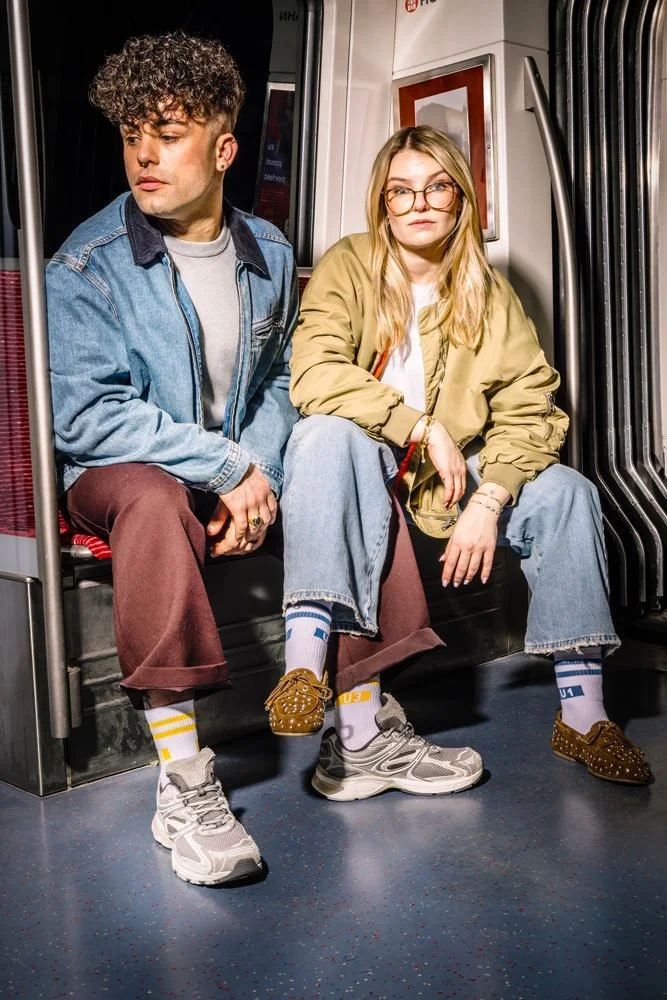 Zwei Models sitzen im Innenraum einer Hamburger U-Bahn und tragen Hochbahn-Socken.