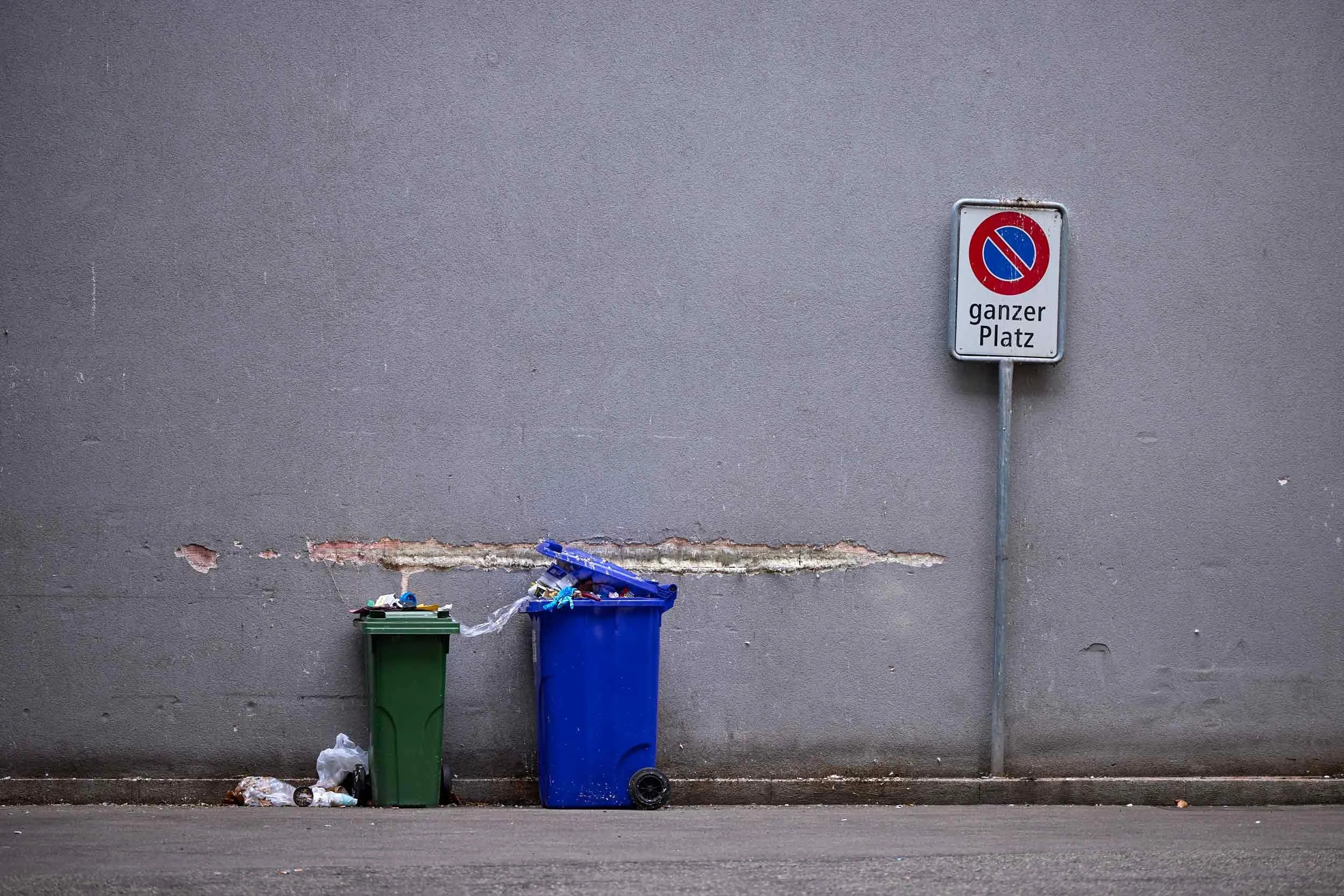 Halteverbotsschild mit Zusatz „ganzer Platz“ an einer Wand, davor zwei Mülltonnen in Basel