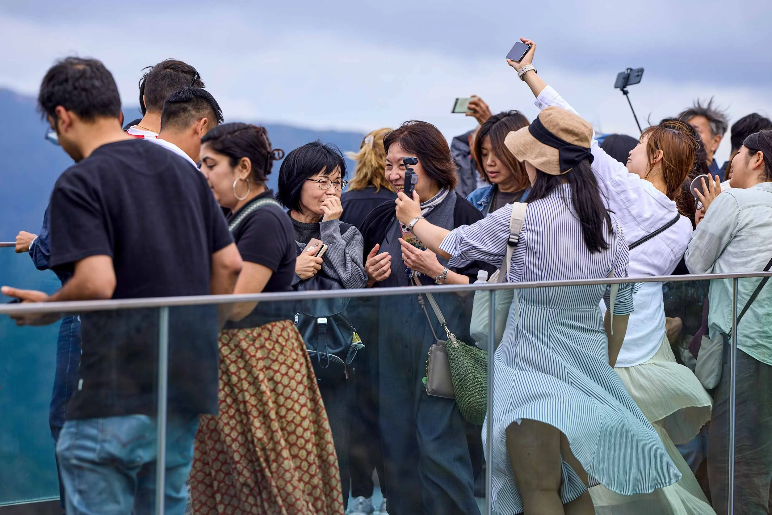 Gruppe von Menschen steht an einem Aussichtspunkt in Owakudani und nutzt Smartphones zum Fotografieren, Berglandschaft im Hintergrund.
