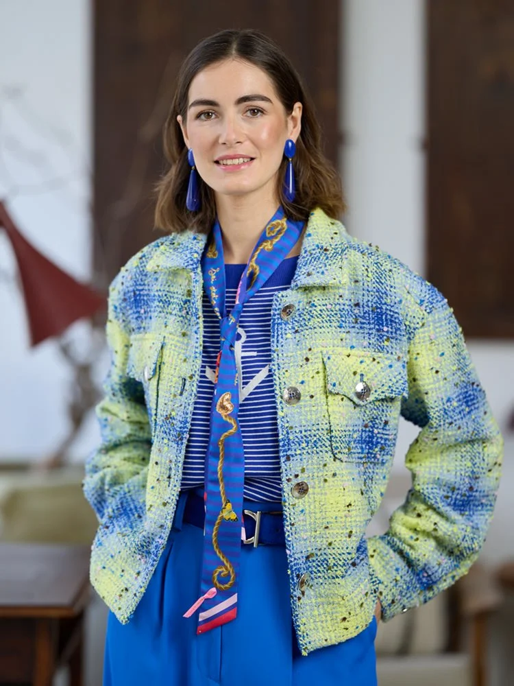 Frau mit blauer Hose, gestreiftem Oberteil und heller Tweedjacke im Innenraum