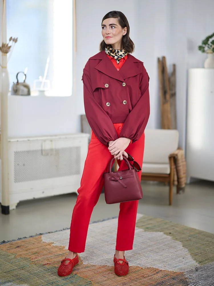 Frau in rotem Outfit mit Handtasche und gemustertem Halstuch im Innenraum