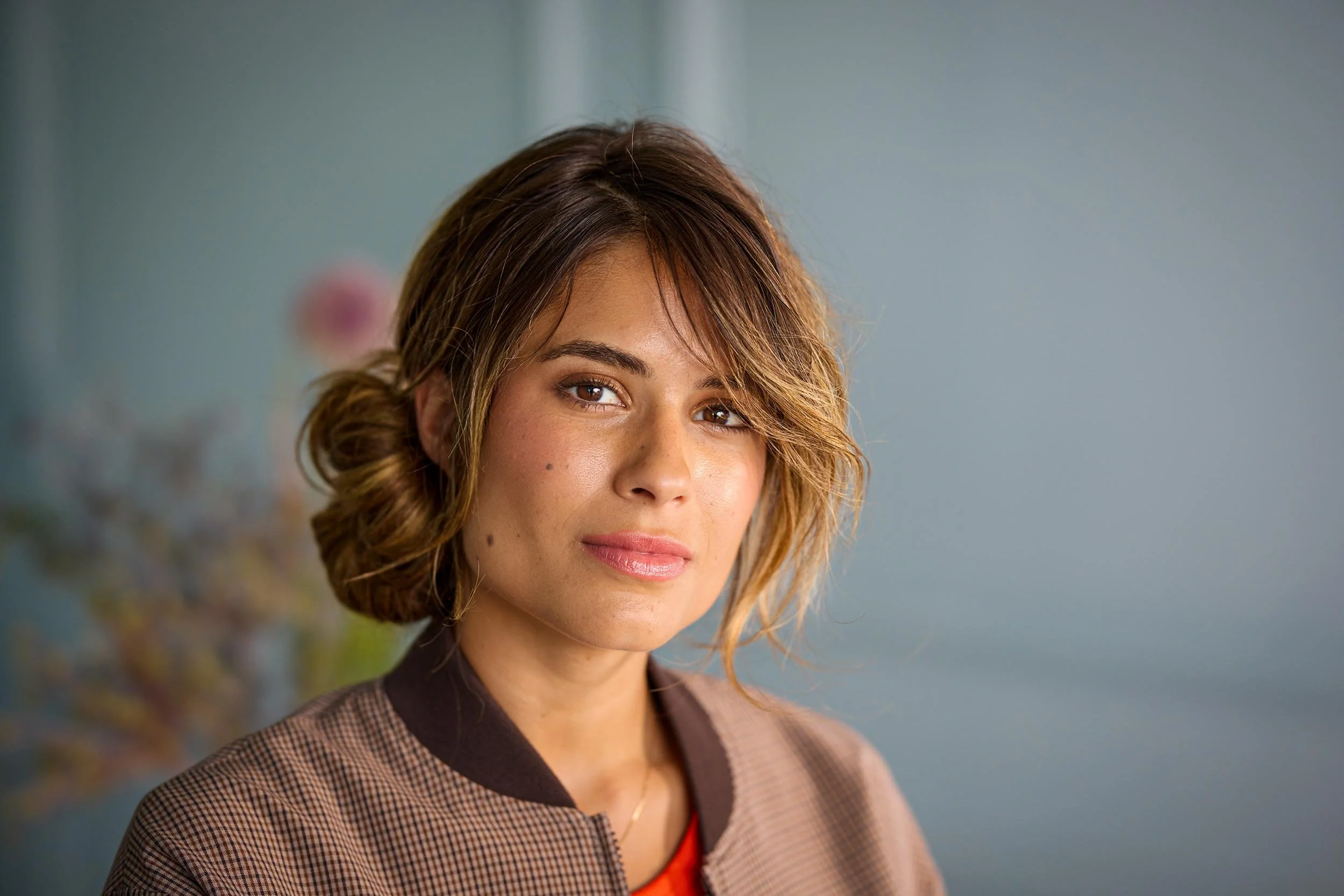 Porträt einer Frau mit locker gebundenem Haar und dezentem Make-up vor hellem Hintergrund.