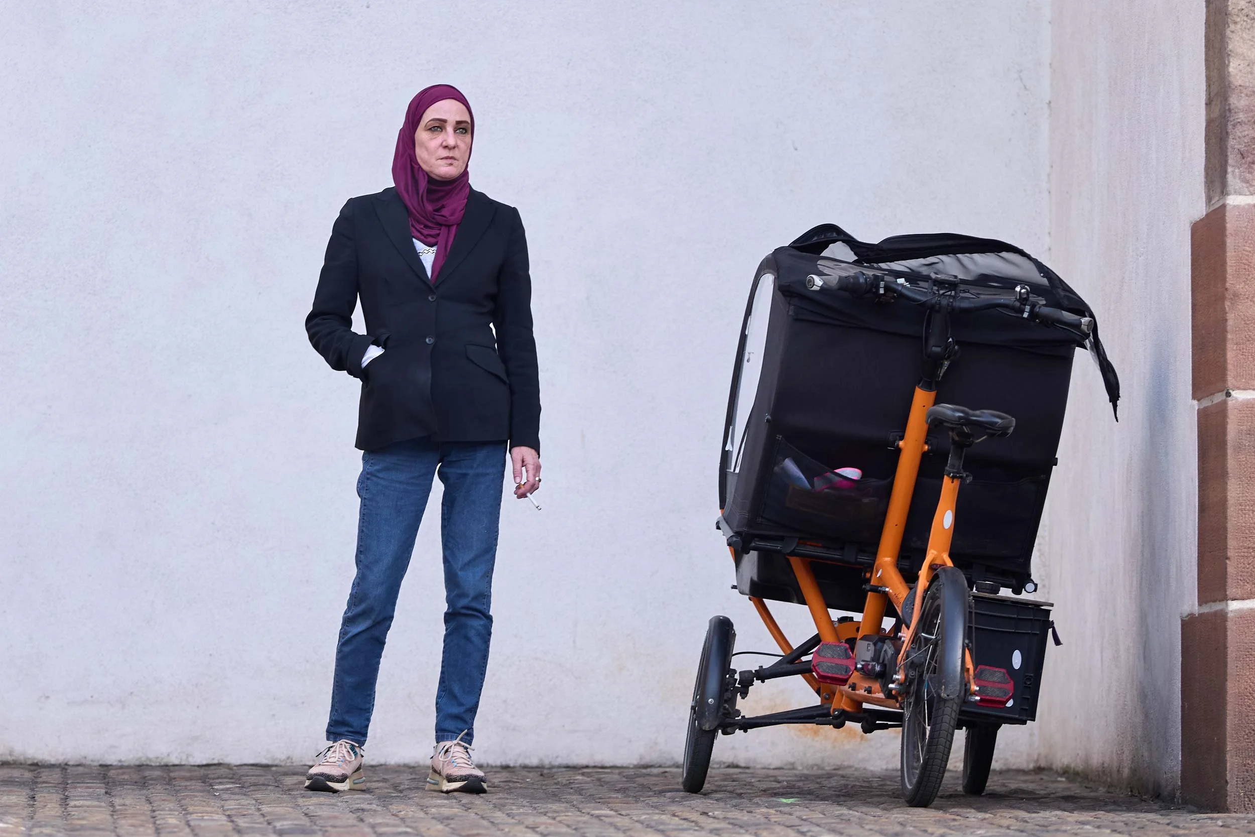 Eine Frau mit Kopftuch steht vor einer Wand neben einem abgestellten Lastenvelo.
