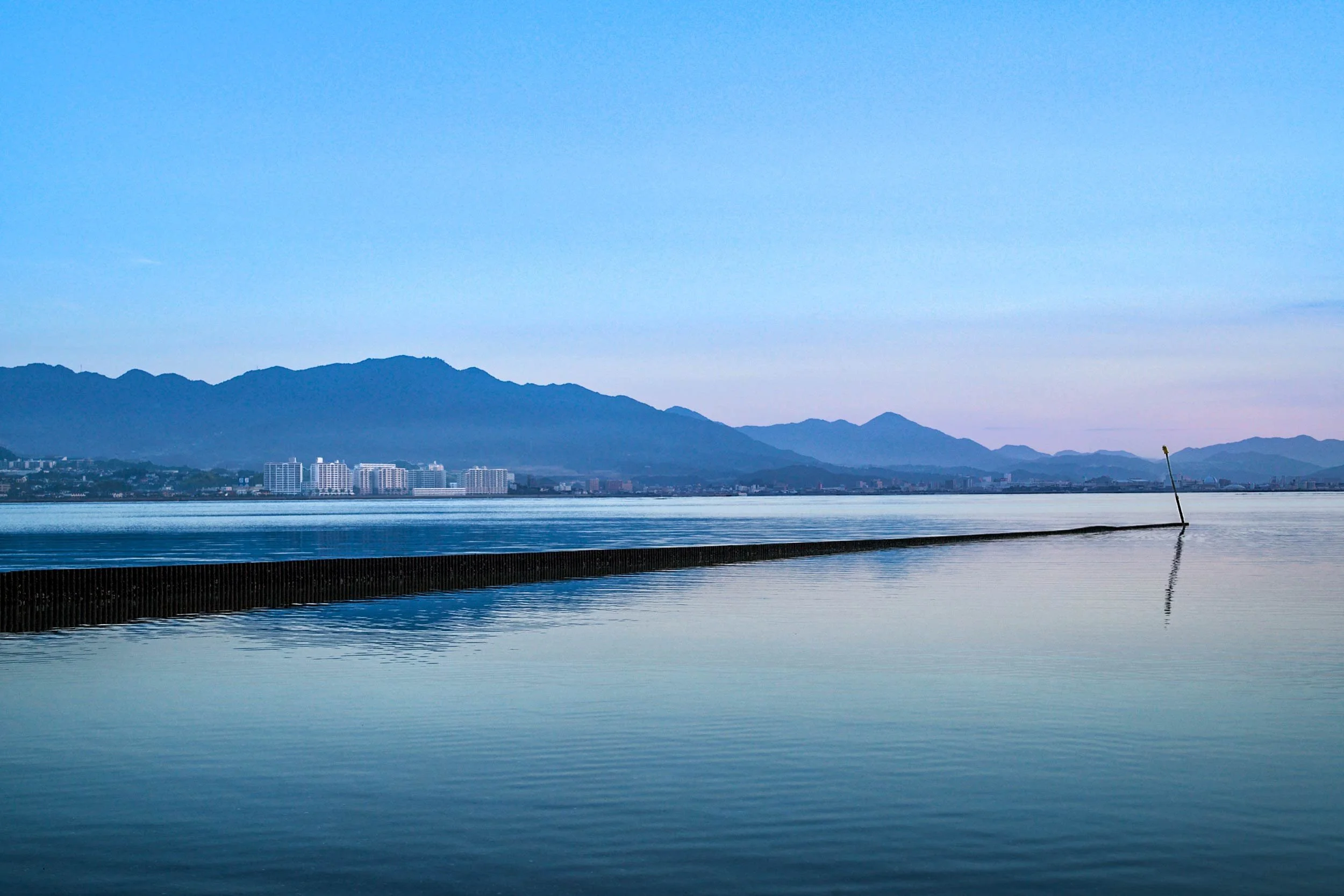 Ruhiges Meer mit langem Damm und Bergsilhouette im Hintergrund auf Miyajima, Japan.