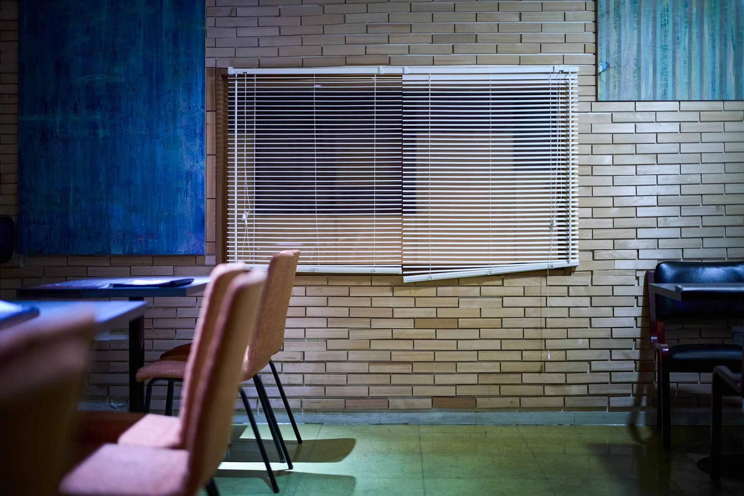 Leerer Innenraum eines Restaurants mit Stühlen, Tischen und Fensterjalousien an einer Kachelwand.