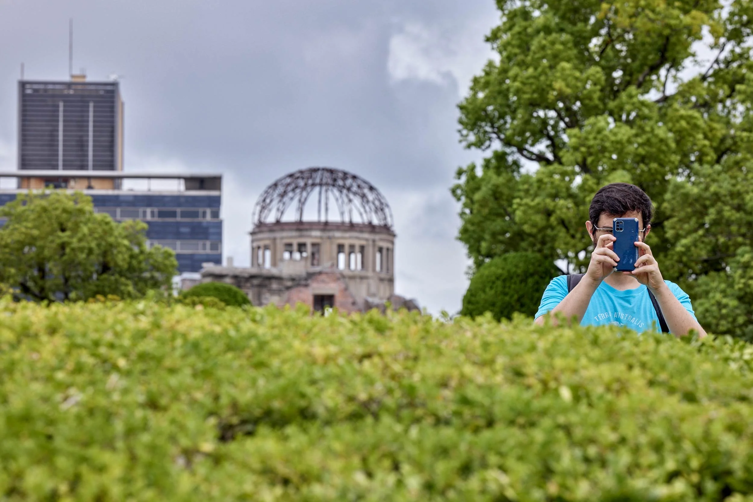 Mann fotografiert mit einem Smartphone, im Hintergrund die Atombombenkuppel in Hiroshima.