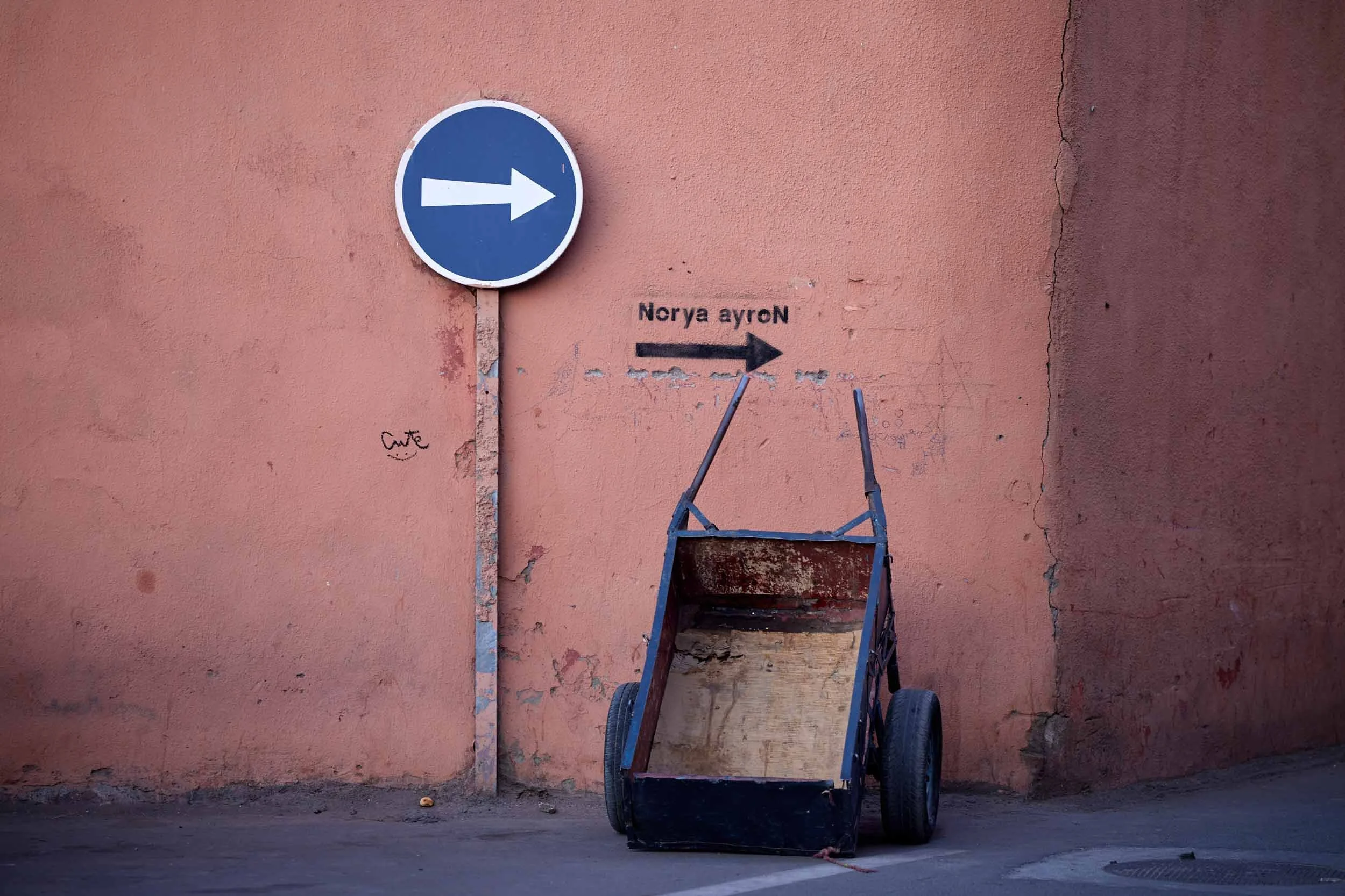 Blaues Verkehrsschild mit weißem Pfeil nach rechts vor einer Wand, daneben ein Handkarren in Marrakesch