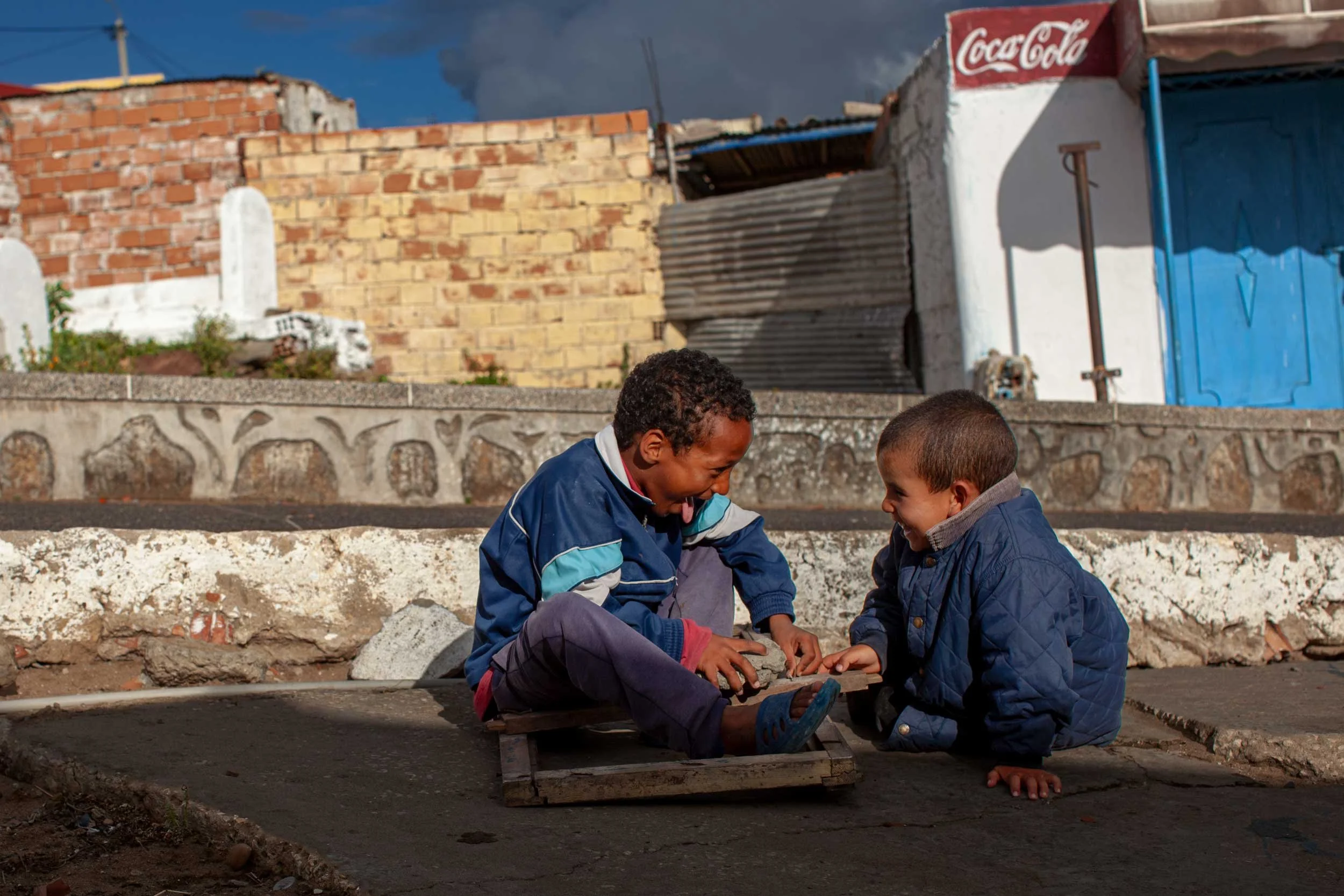 Zwei kinder sitzen auf der strasse und spielen vor haeusern in marokko