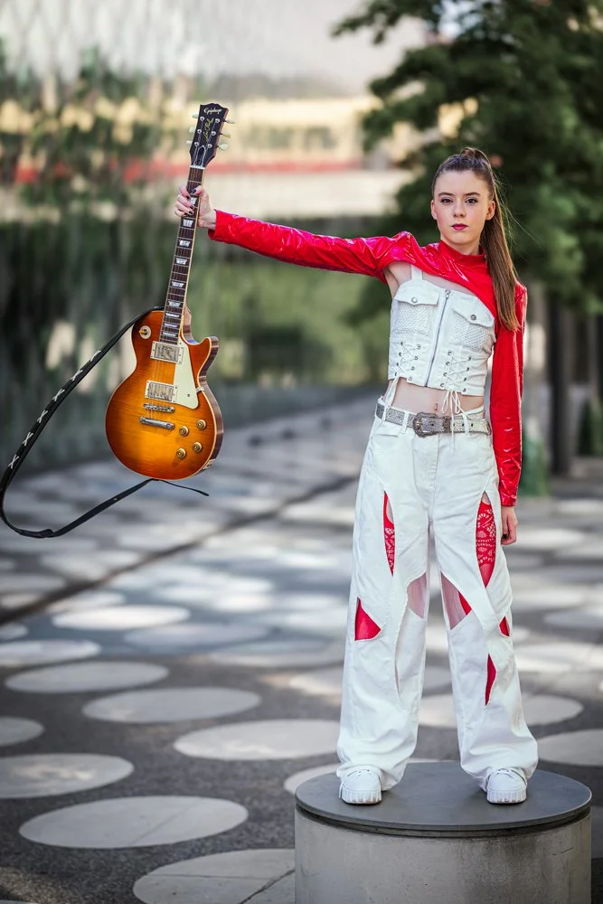Mitglied der Band III RIØT hält eine Epiphone E-Gitarre und steht auf einem Betonsockel vor dem Futurium in Berlin.
