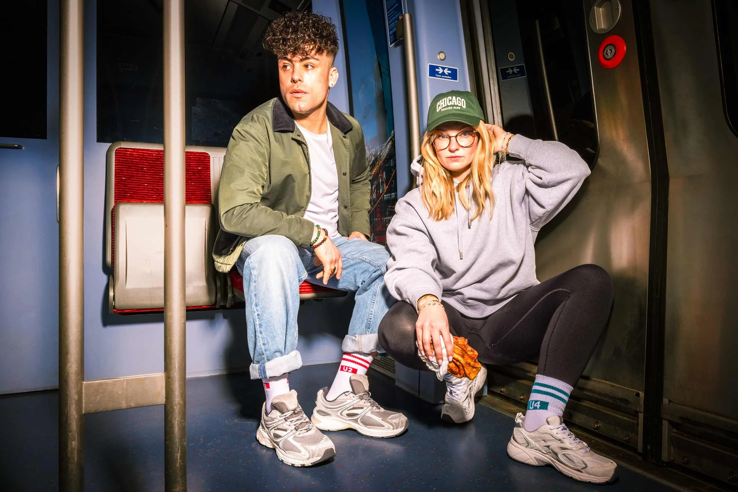 Zwei Models sitzen im Innenraum einer Hamburger U-Bahn und tragen Hochbahn-Socken.