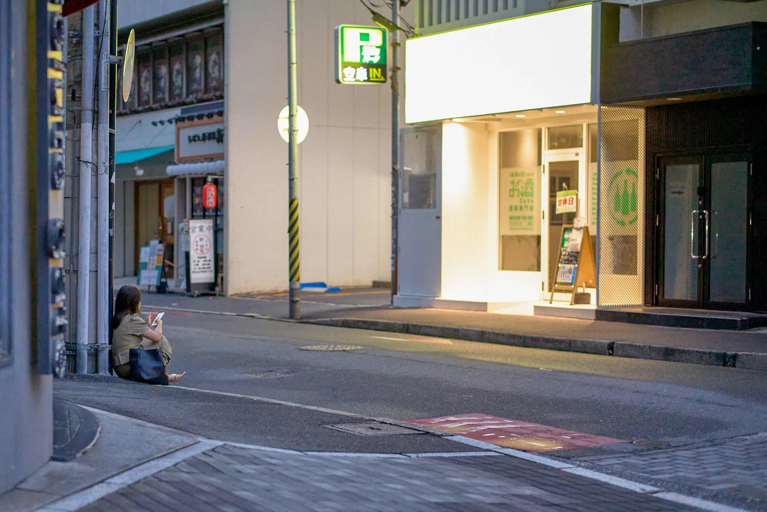 Eine Frau sitzt auf einem Gehweg in Hiroshima und benutzt ihr Smartphone.