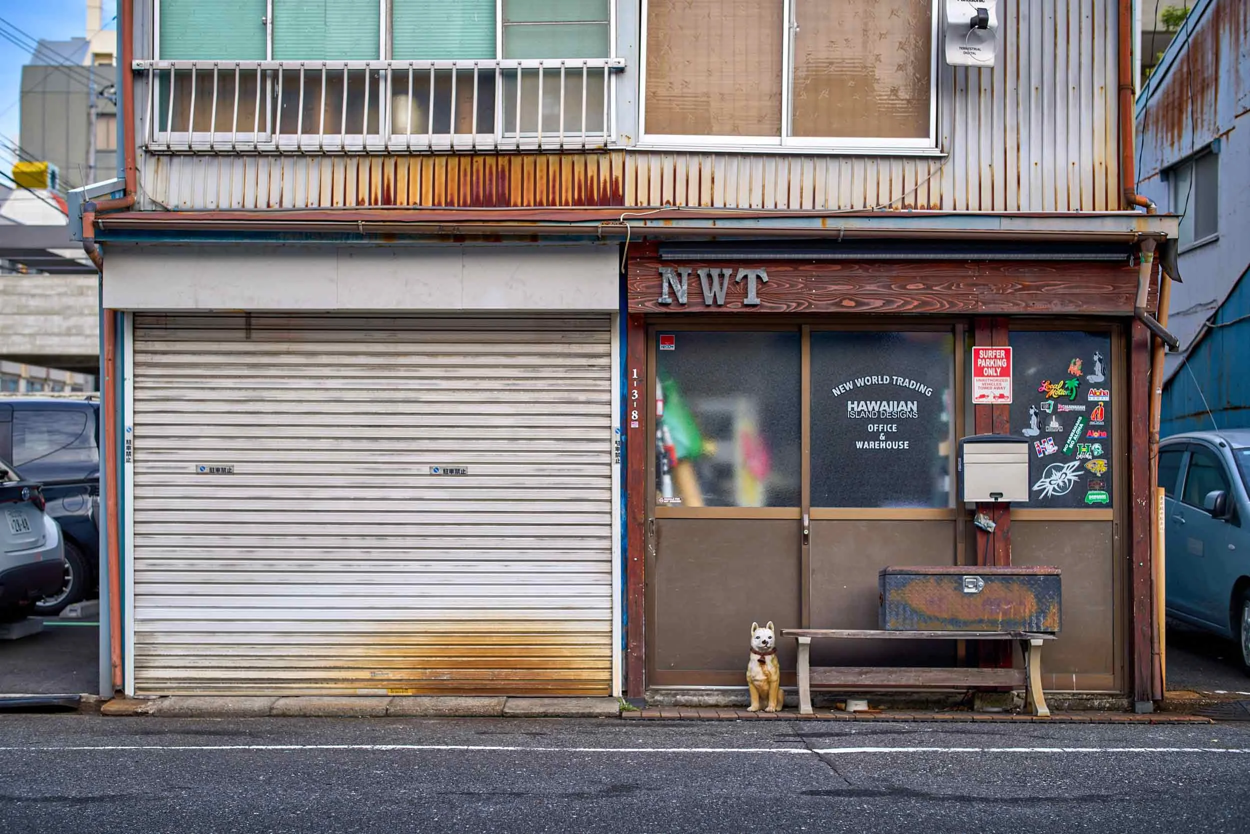 Shiba-Inu-Hundefigur sitzt vor einer Geschäftsfassade mit Rollladen und Eingang in Tokio.
