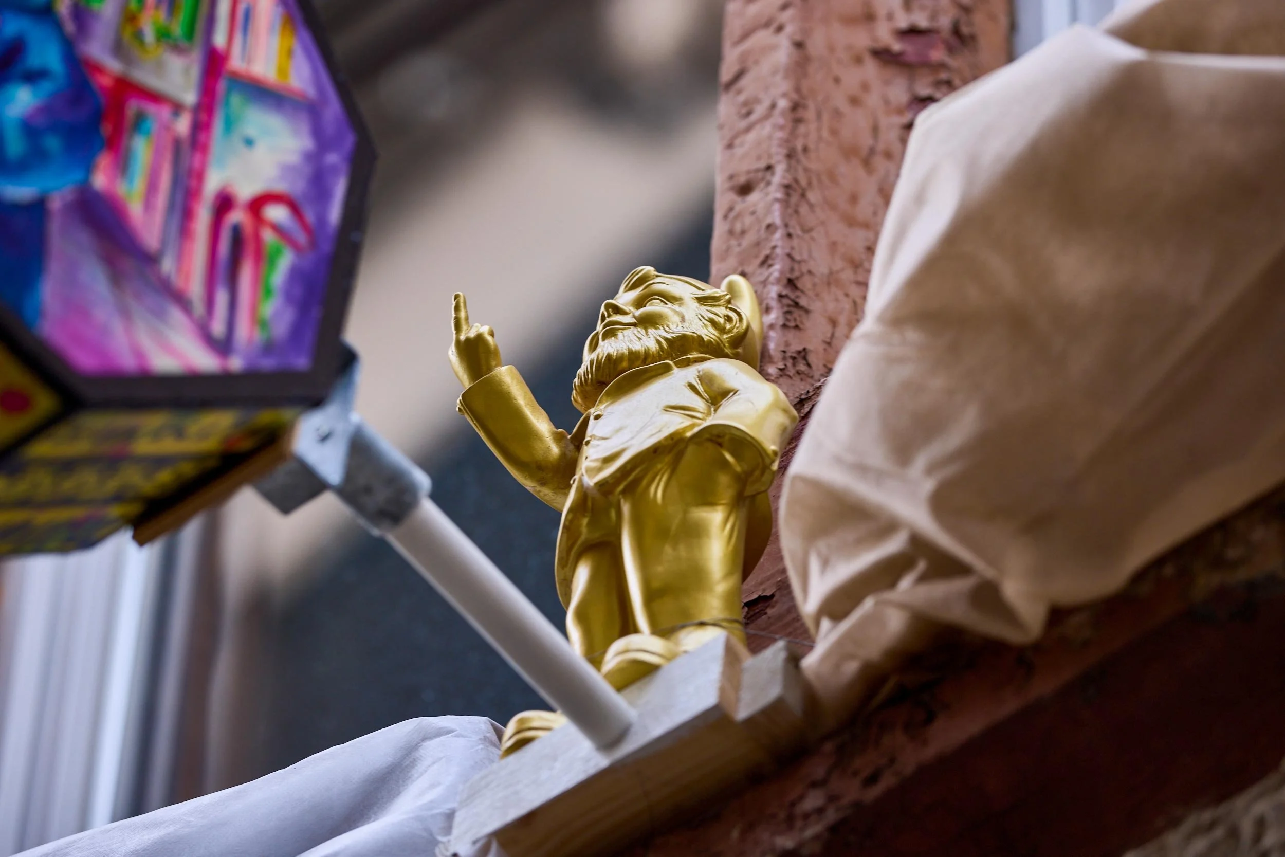 Goldene kleine Figur auf einem Fenstersims neben einem Verkehrsschild an einer Hausfassade in Basel.