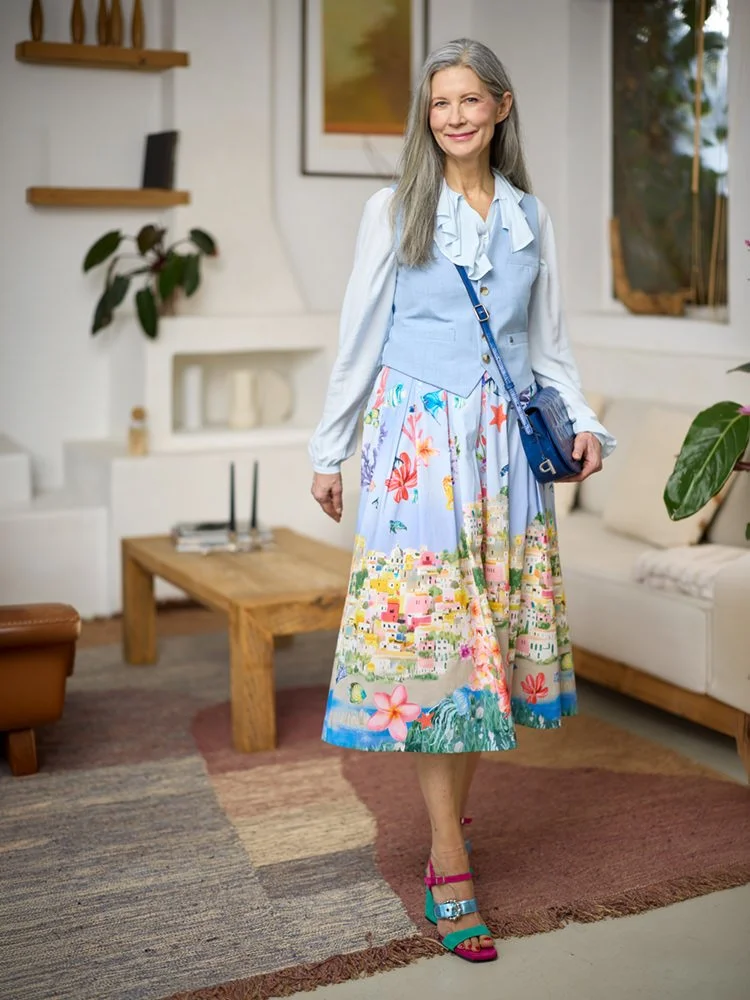 Ältere Frau mit hellblauer Bluse und gemustertem Rock im Wohnzimmer