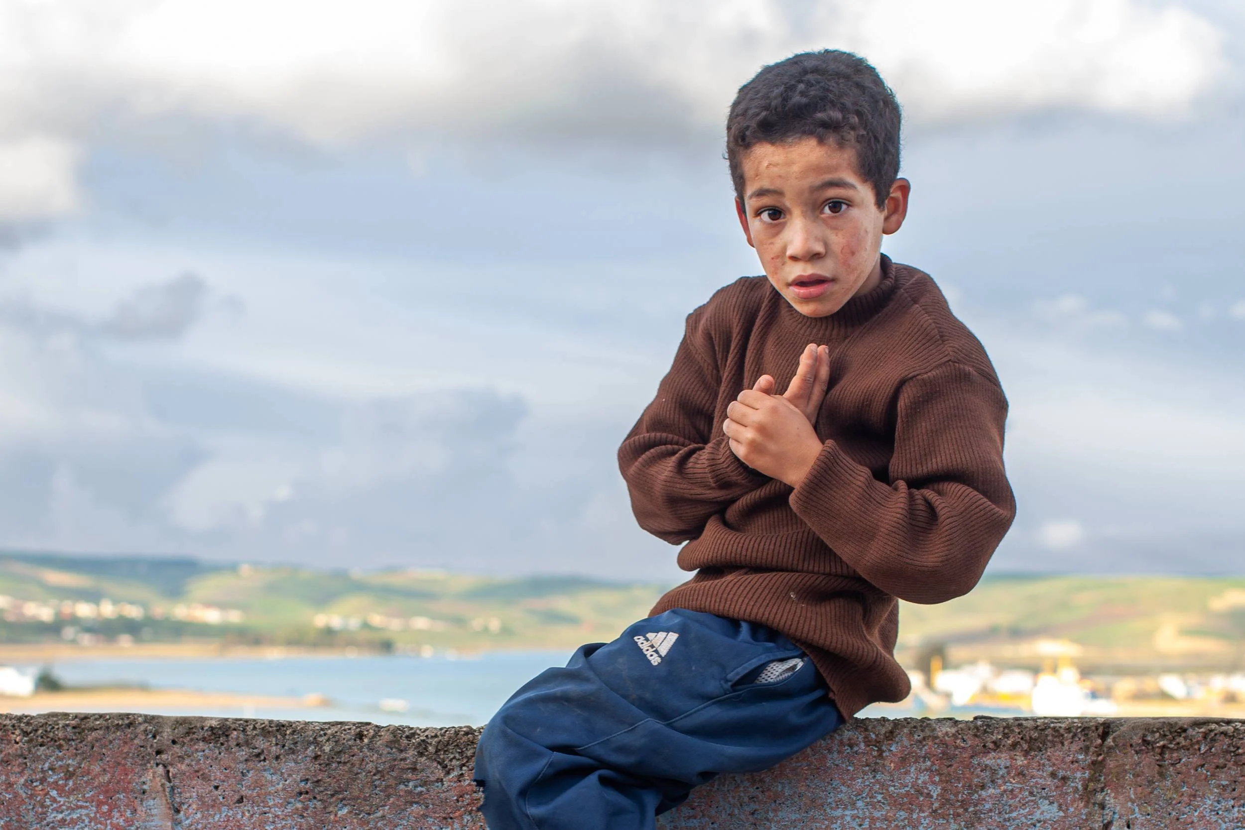 Junge sitzt auf einer mauer vor kuestenlandschaft in marokko