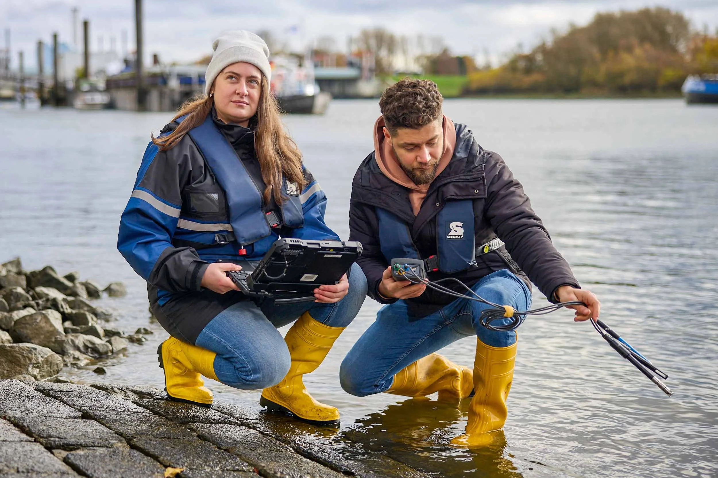 Zwei Fachkräfte bei einer Wasseranalyse am Hafen mit Messgeräten und Tablet