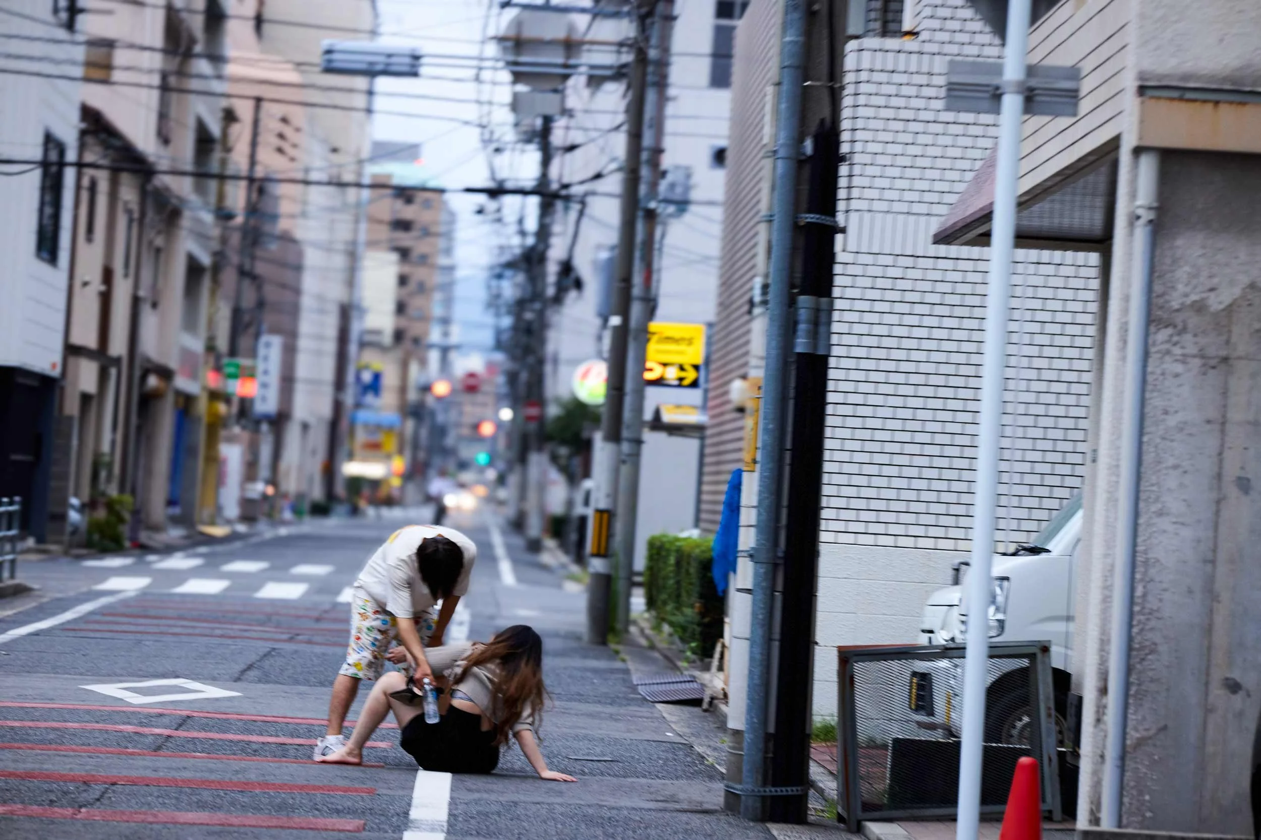 Zwei Personen befinden sich auf einer Strasse in Hiroshima, eine Person sitzt auf dem Boden, die andere steht daneben.
