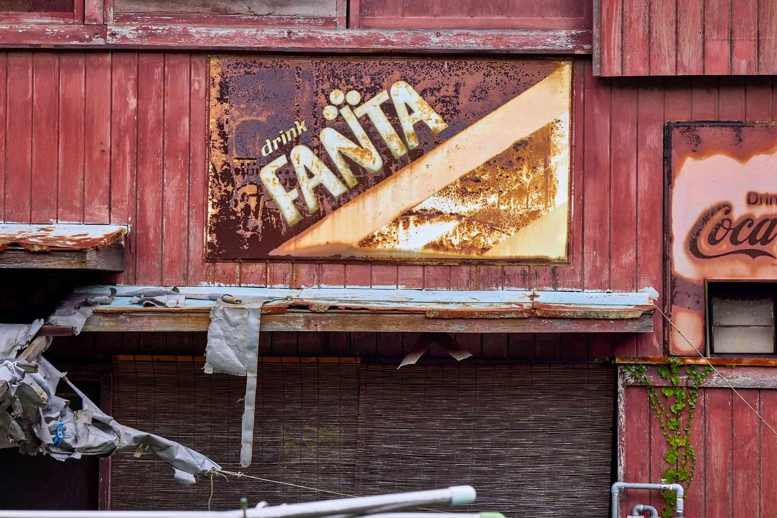 Verblasste Coca-Cola-Werbung an einer roten Holzfassade eines Gebäudes in Naoshima