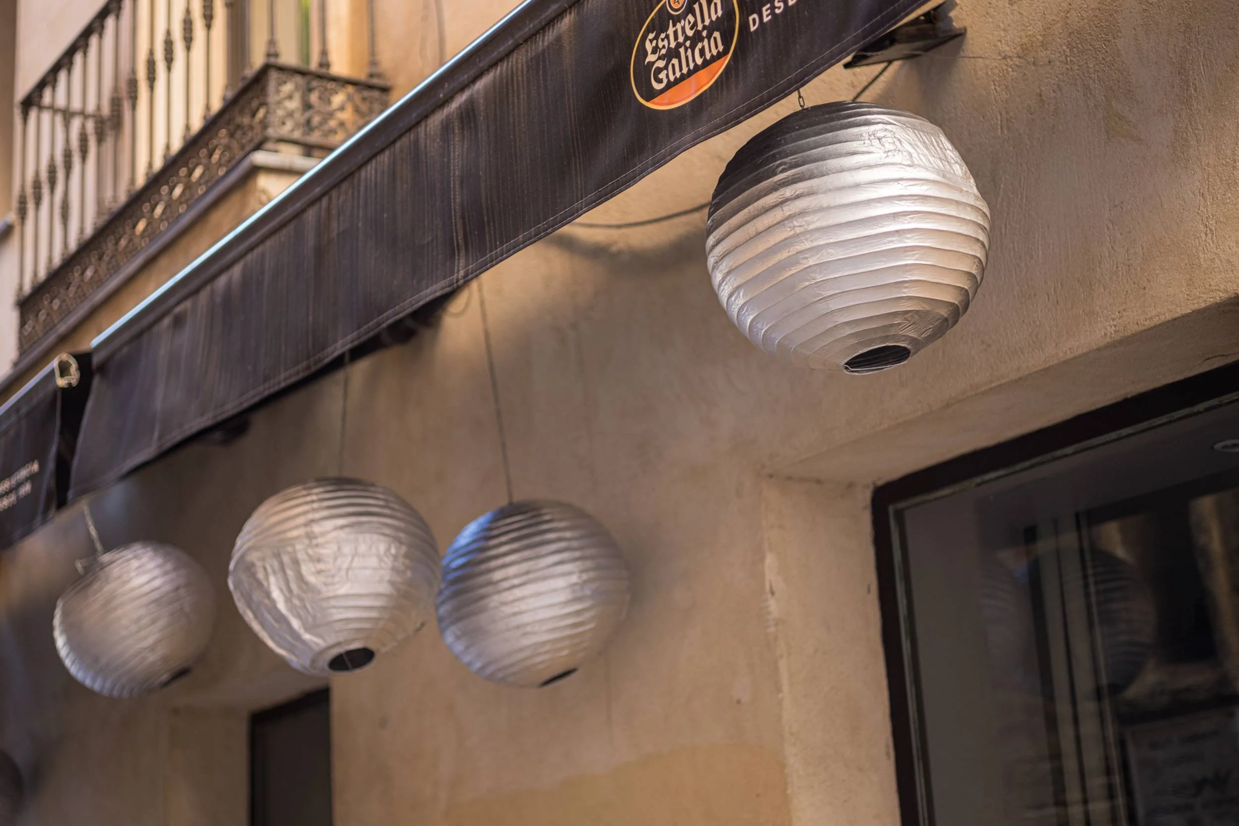 Mehrere weisse papierlaternen haengen unter einem vordach an einer cafe fassade in sevilla