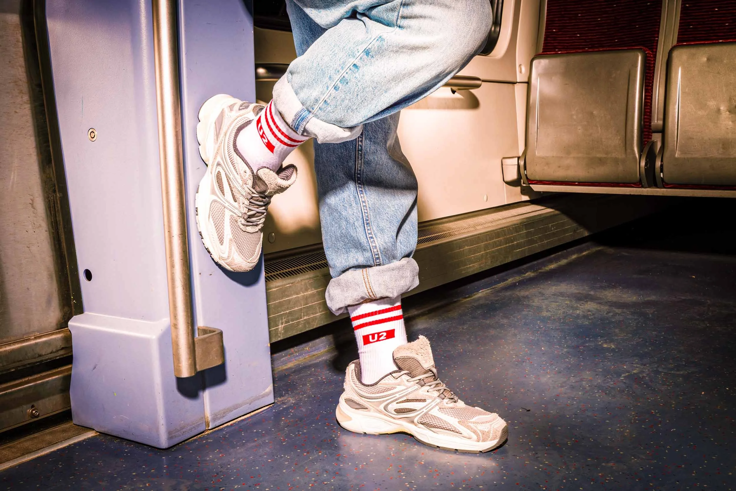Person mit Jeans, weißen Sneakern und Hochbahn-Socken steht im Innenraum einer Hamburger U-Bahn.