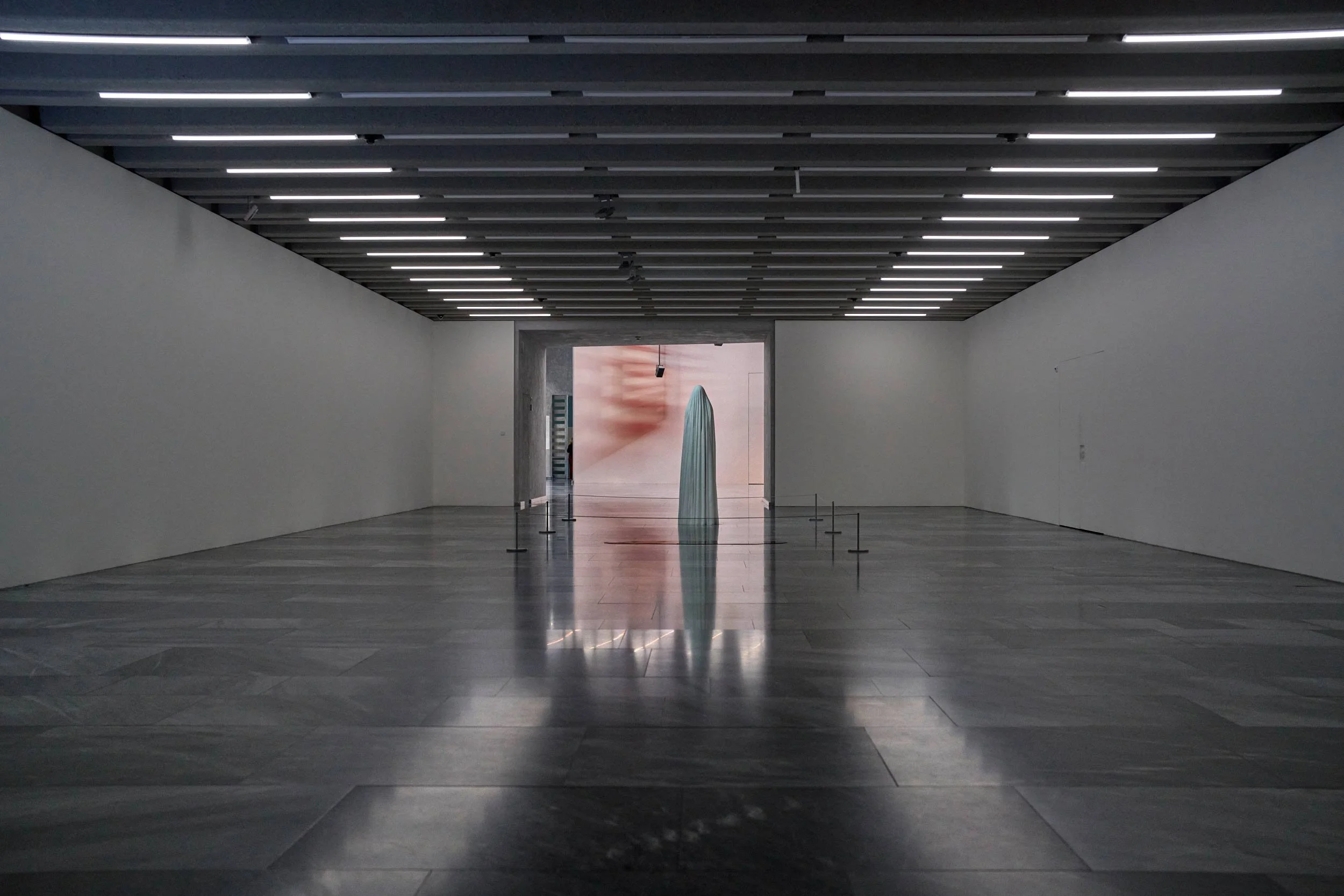 Grosse Ausstellungshalle mit glattem Boden, Deckenleuchten und einer Installation im Hintergrund.Geist und Blutlache“ von Katharina Fritsch,