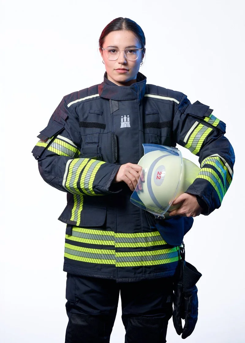 Feuerwehrfrau in Einsatzkleidung mit Feuerwehrhelm vor hellem Hintergrund