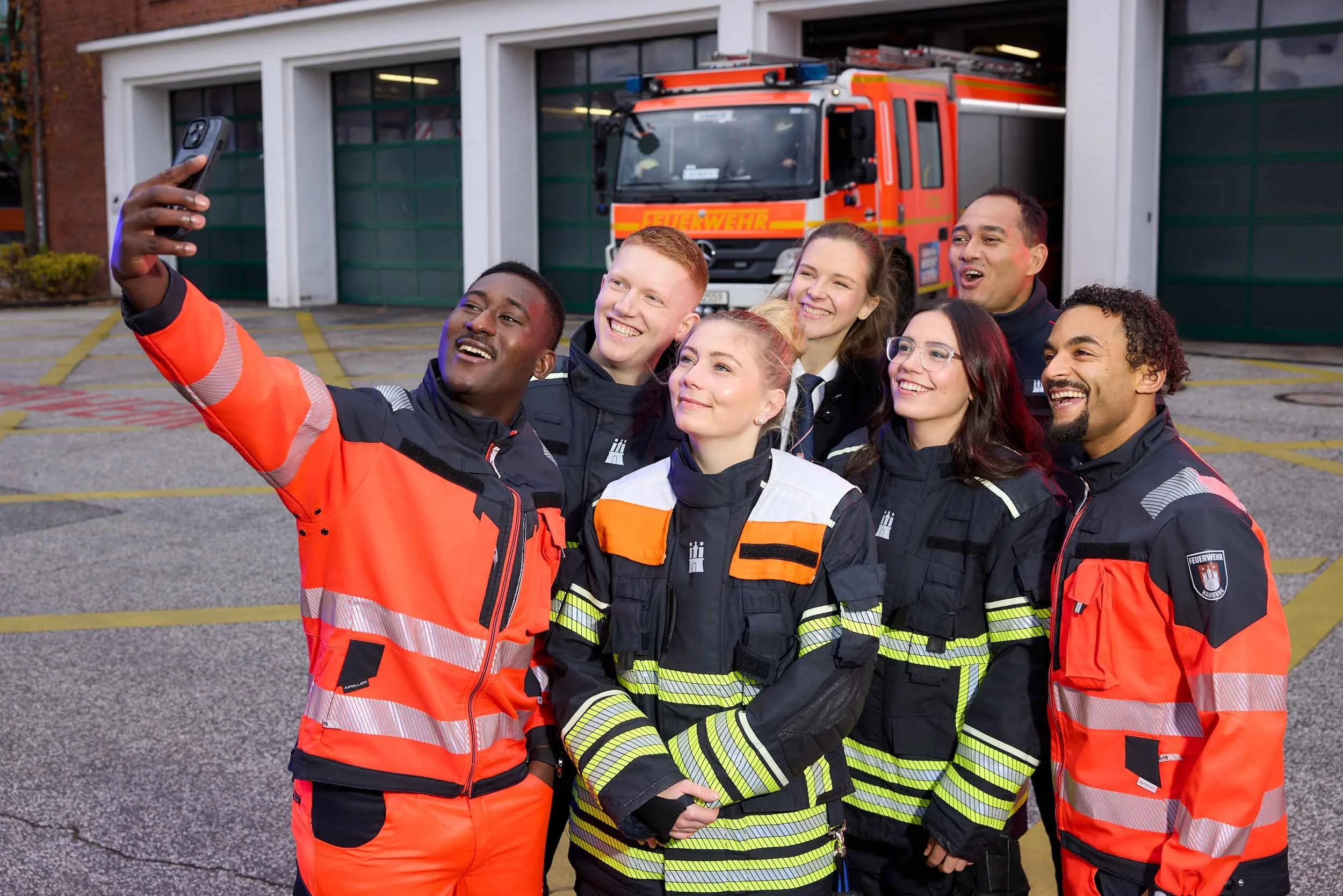 Feuerwehrteam macht ein Selfie vor einem Feuerwehrfahrzeug auf dem Feuerwehrgelände